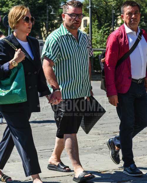 黒無地のメガネ、グリーン・白ストライプのシャツ、黒無地のショートパンツ、プラダの黒シャワーサンダル、黒小紋のクラッチバッグ/セカンドバッグ/巾着を合わせた夏春のメンズコーデ・着こなし。