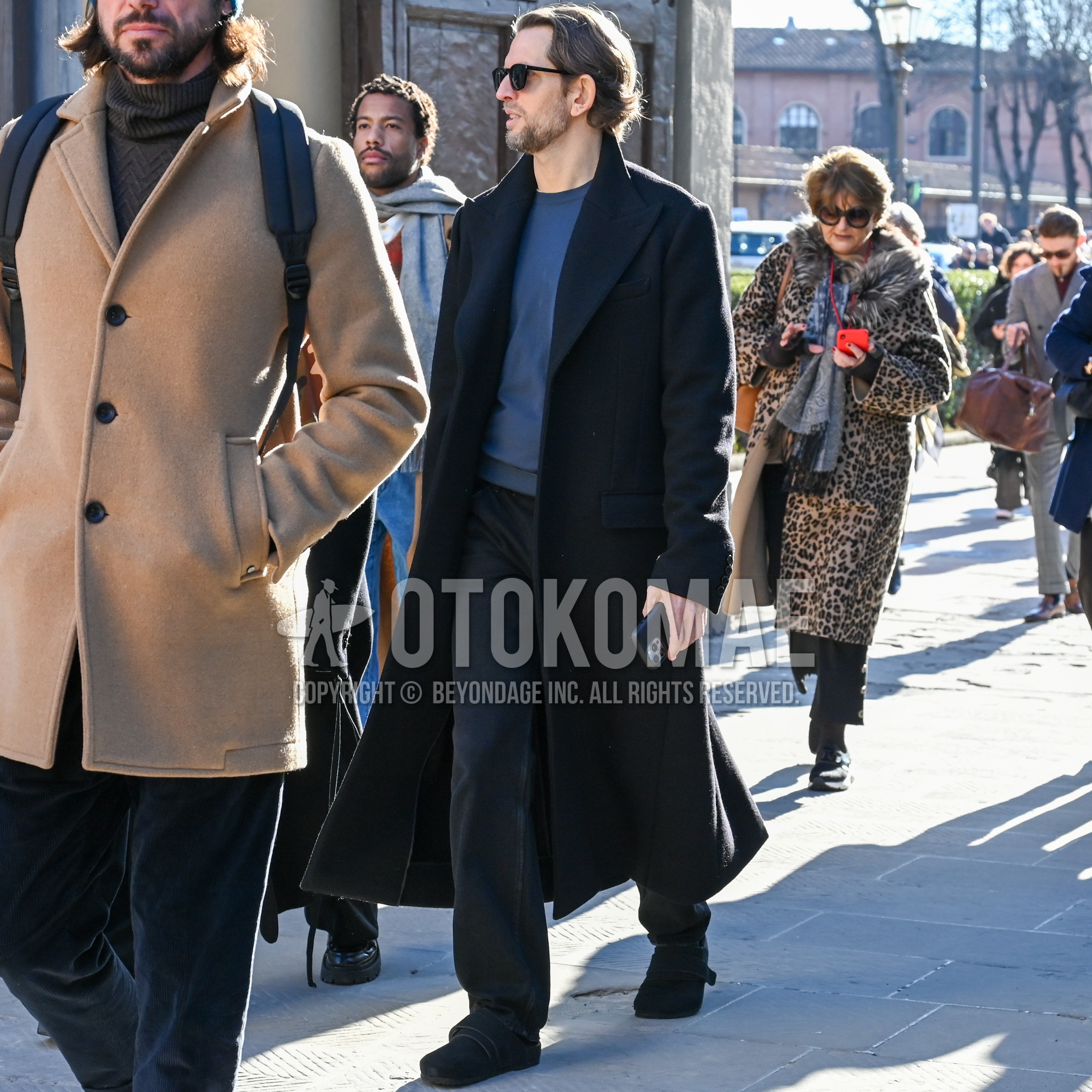 Men's autumn winter outfit with black plain sunglasses, black plain chester coat, blue plain sweater, dark gray plain denim/jeans, black suede shoes leather shoes.