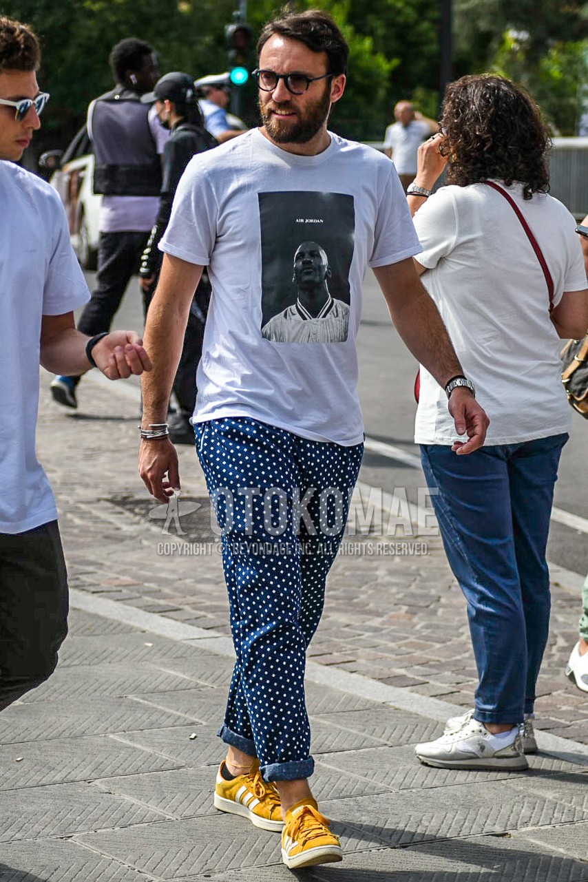 Men's summer outfit with black plain glasses, white graphic t-shirt, navy dots cotton pants, yellow low-cut sneakers.