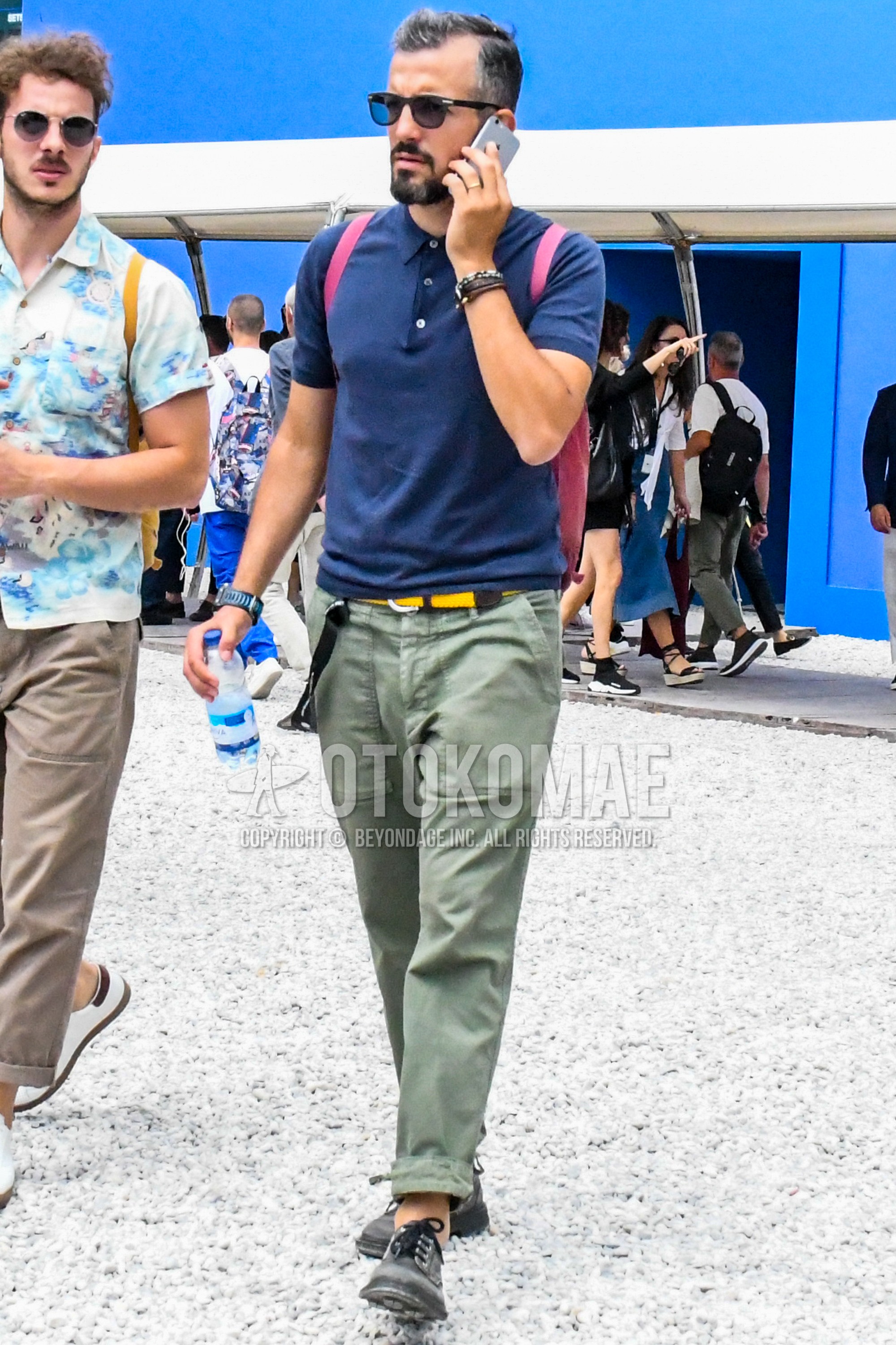 Men's spring summer outfit with black plain sunglasses, navy plain polo shirt, yellow plain braided belt, olive green plain chinos, black plain toe leather shoes.