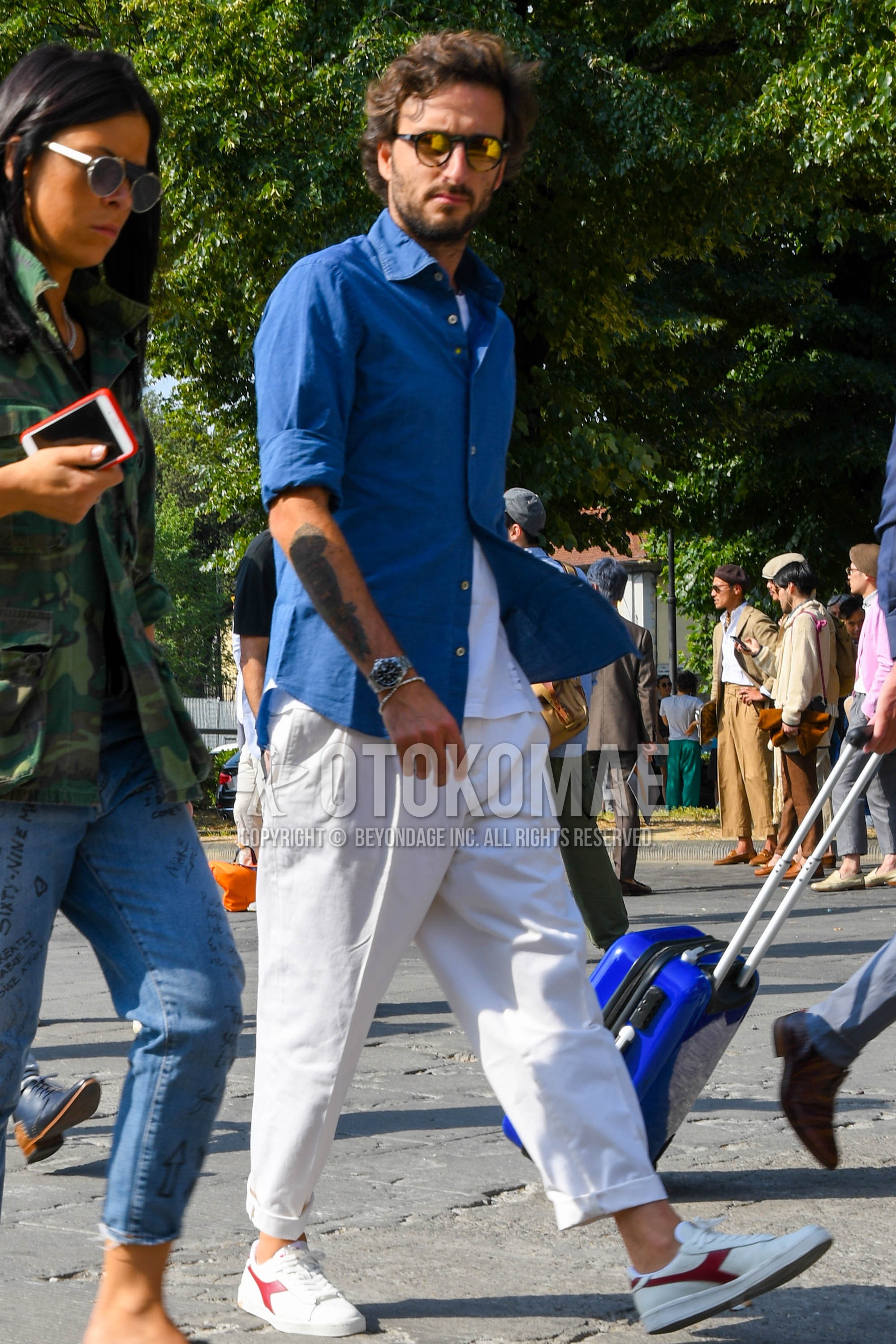 Men's spring summer outfit with plain sunglasses, blue plain shirt, white plain t-shirt, white plain cotton pants, plain pleated pants, white low-cut sneakers.