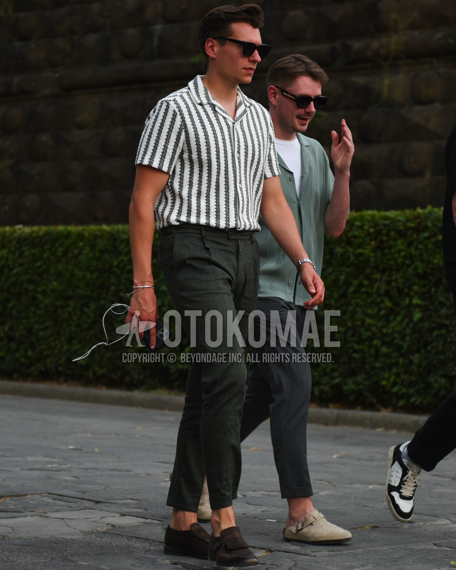 Men's spring summer outfit with black plain sunglasses, olive green white stripes shirt, olive green plain slacks, brown monk shoes leather shoes, brown suede shoes leather shoes.