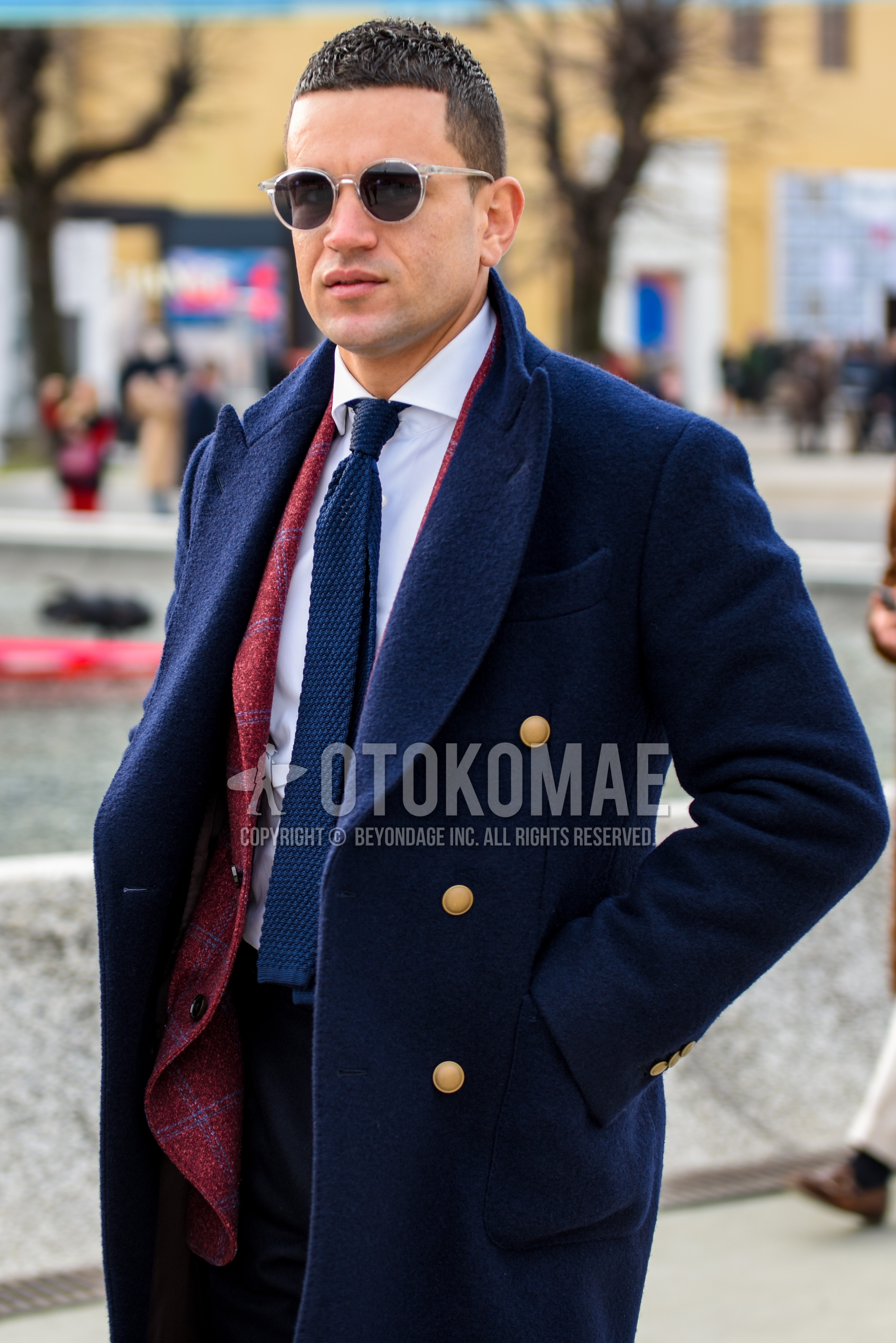 Men's autumn winter outfit with clear plain glasses, navy plain chester coat, white plain shirt, red check tailored jacket, navy plain knit tie.