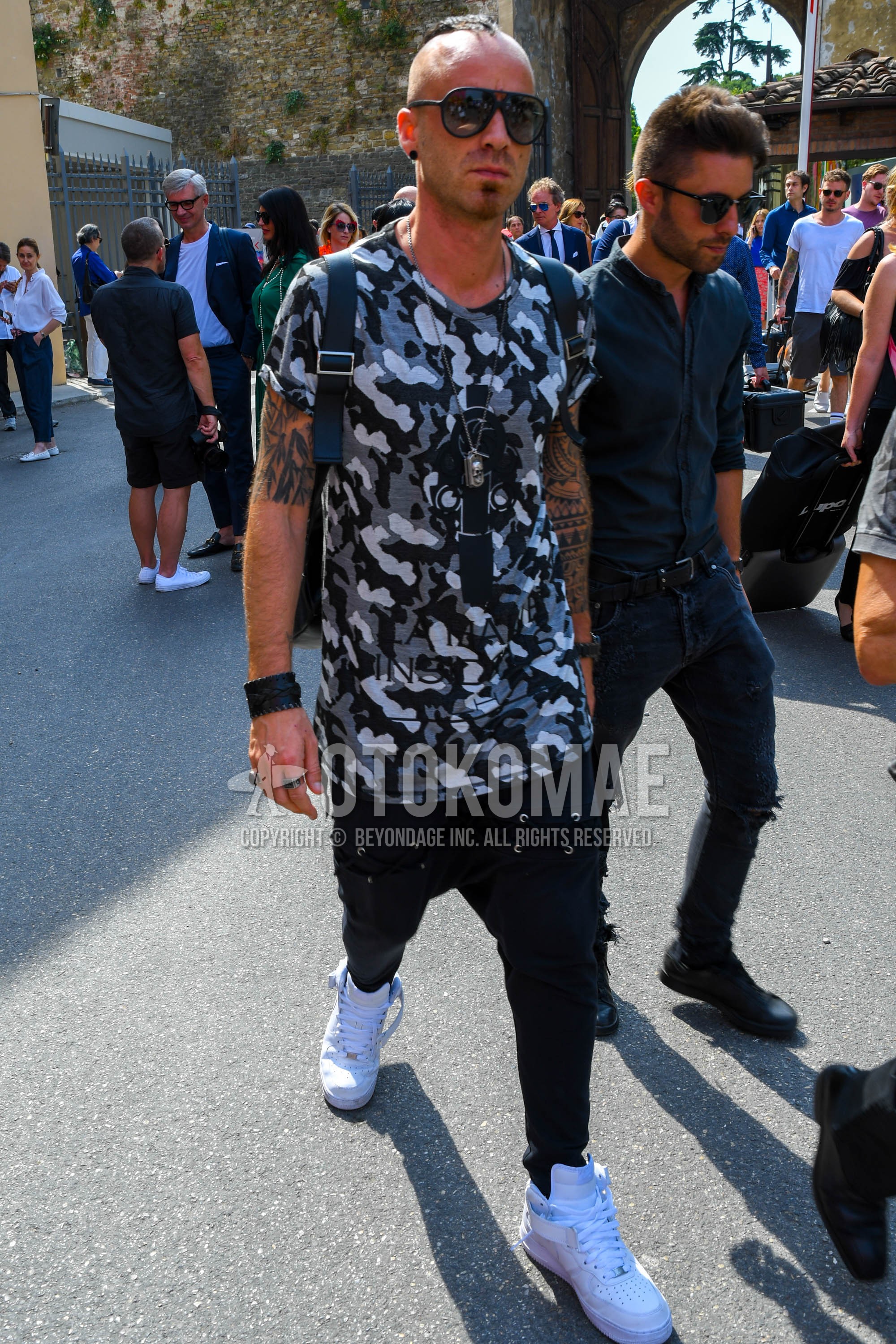 Men's summer outfit with plain sunglasses, white black camouflage t-shirt, black plain denim/jeans, white high-cut sneakers.
