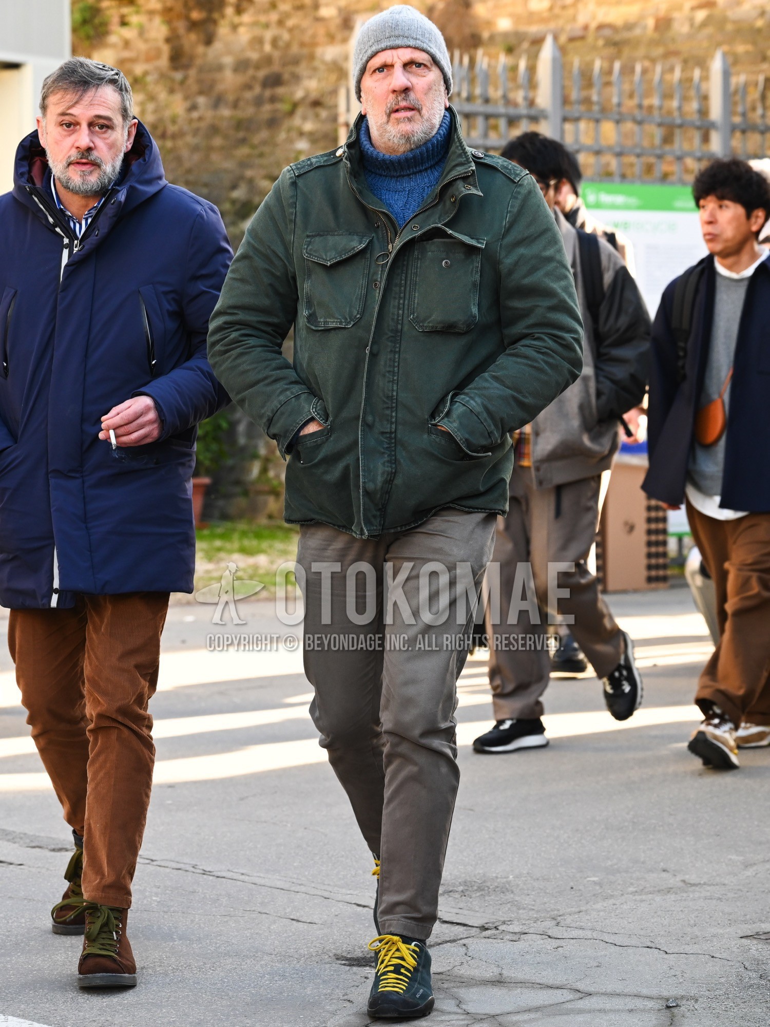Men's autumn winter outfit with gray plain knit cap, olive green plain field jacket/hunting jacket, blue plain turtleneck knit, gray plain cotton pants, black low-cut sneakers.