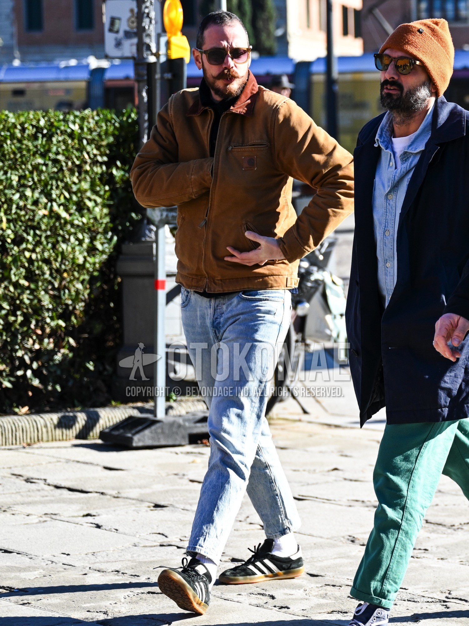 Men's autumn winter outfit with brown plain sunglasses, brown beige plain coverall, black plain t-shirt, blue plain denim/jeans, white plain socks, black low-cut sneakers.