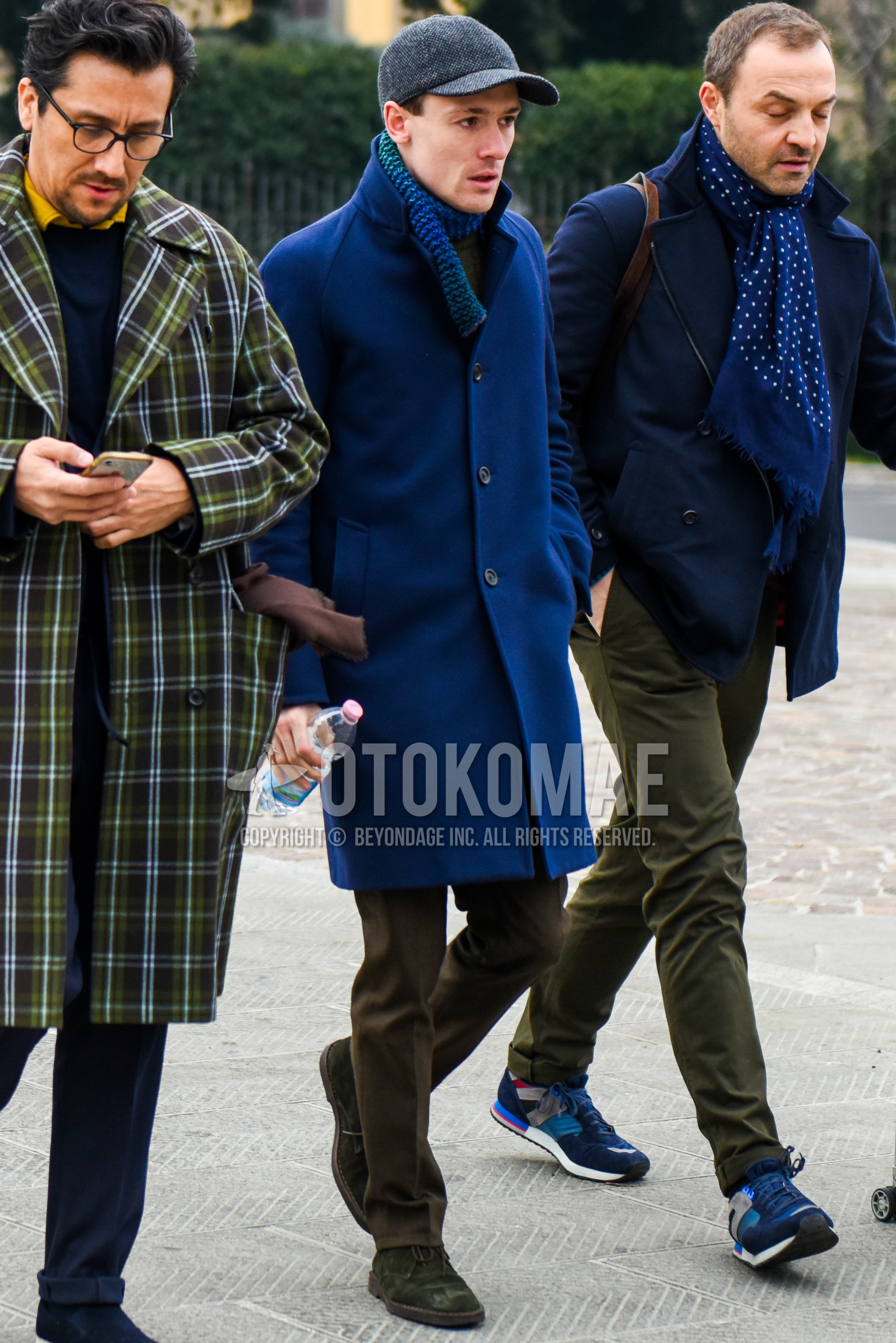 Men's autumn winter outfit with gray herringbone baseball cap, blue scarf scarf, navy plain stenkarrer coat, brown plain slacks, olive green chukka boots.