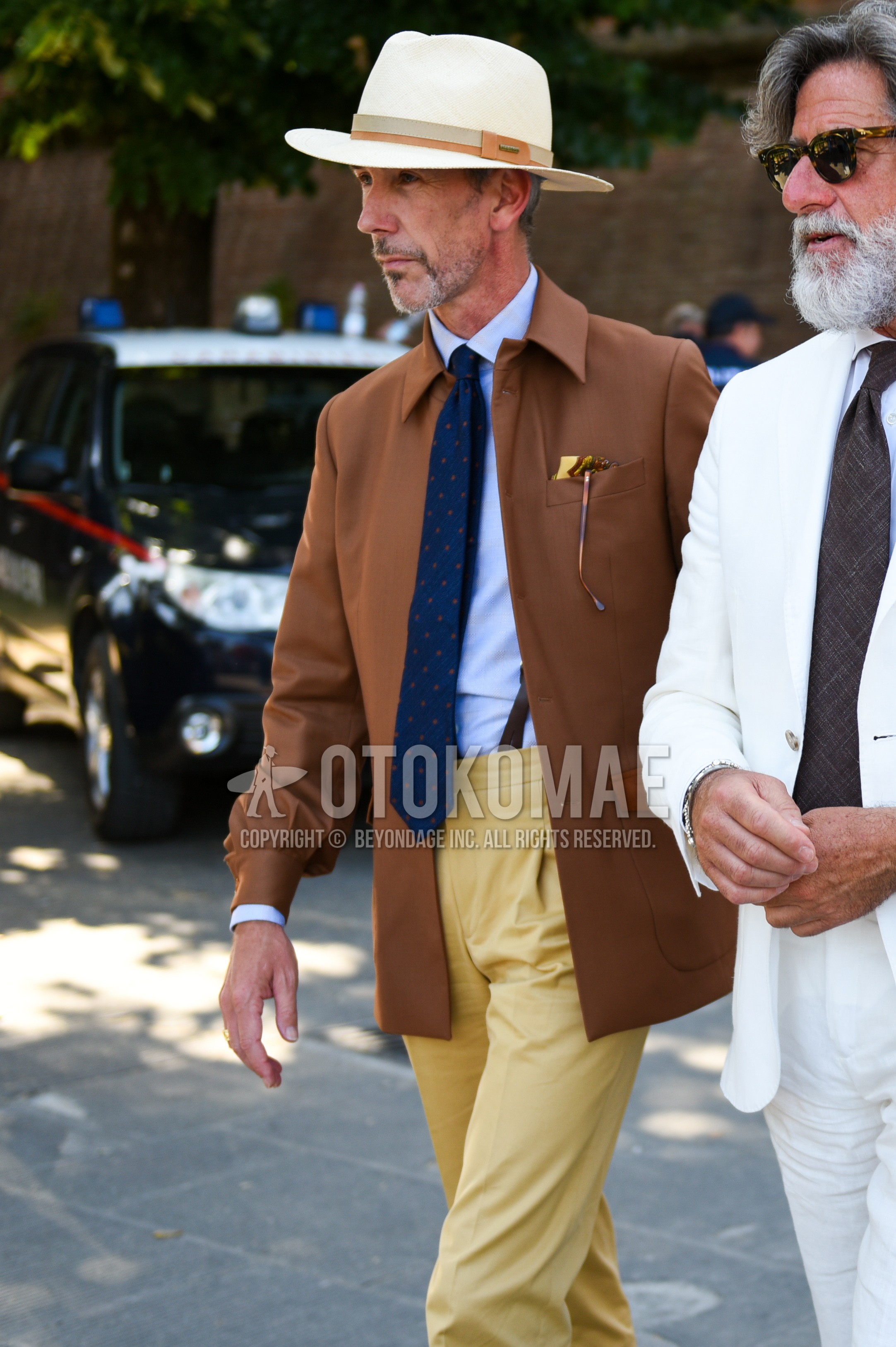 Men's spring autumn outfit with beige plain hat, brown plain shirt jacket, light blue plain shirt, brown plain suspenders, beige plain pleated pants, plain chinos, navy necktie necktie.