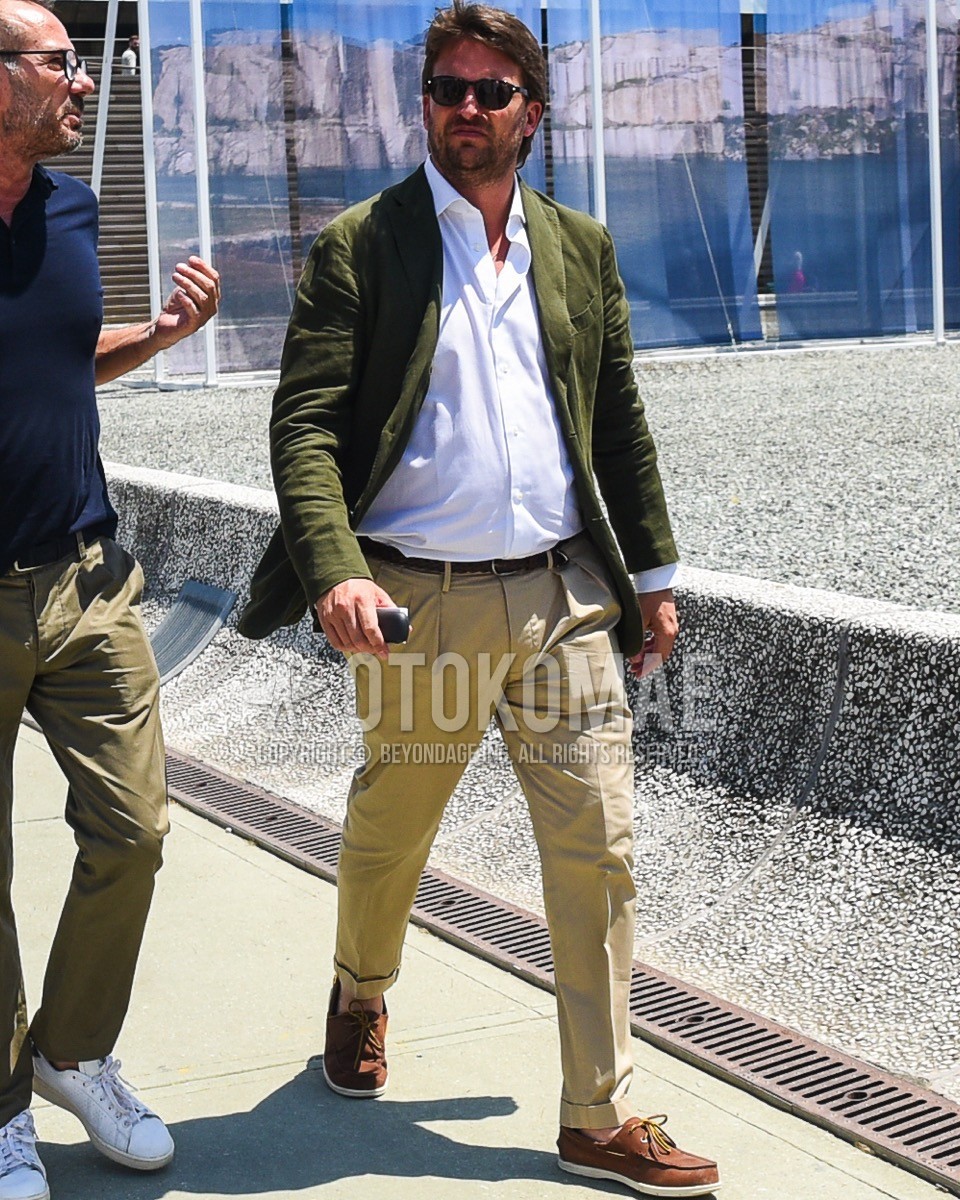 Men's spring summer outfit with black plain sunglasses, olive green plain tailored jacket, white plain shirt, brown plain braided belt, beige plain chinos, brown moccasins/deck shoes leather shoes.
