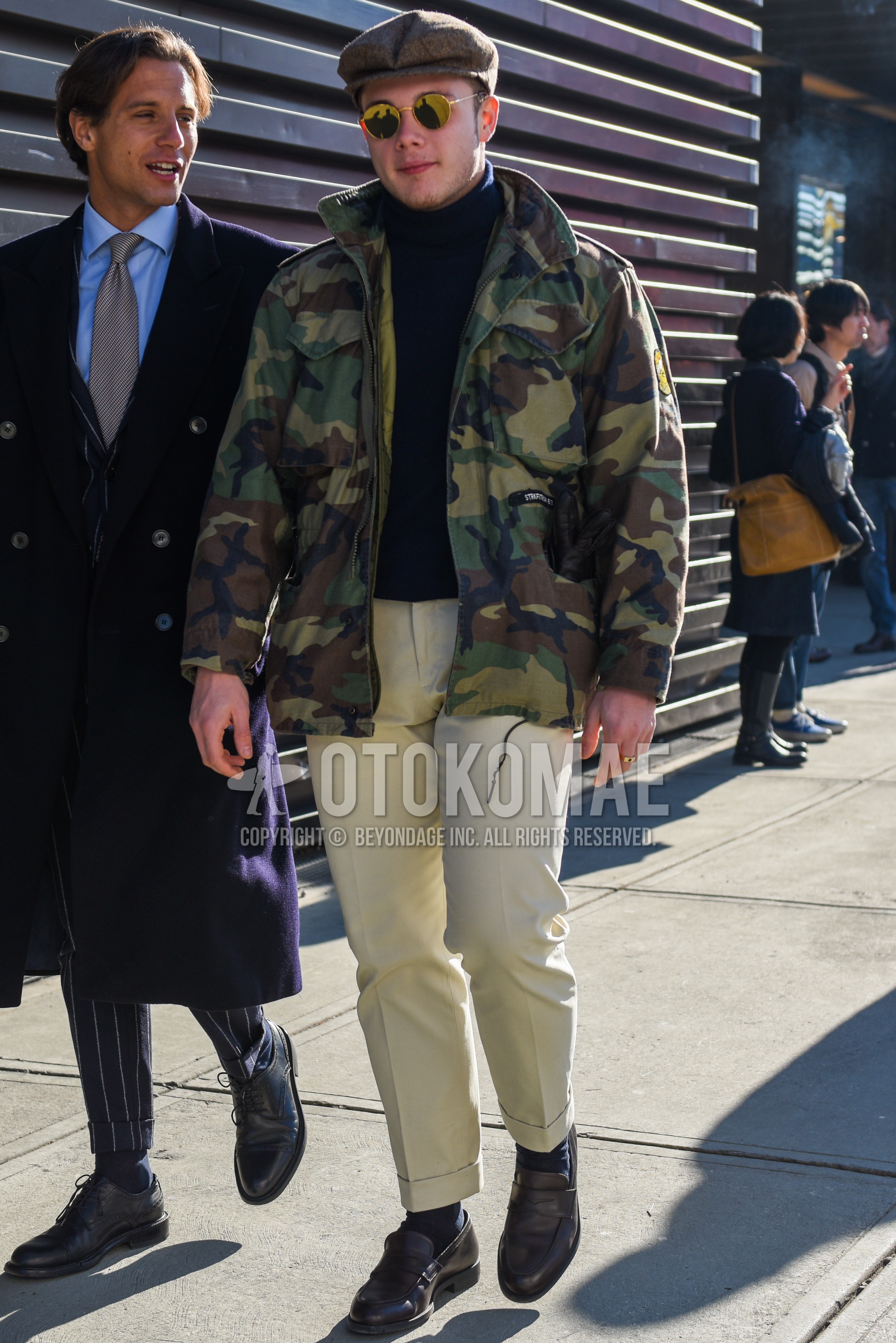 Men's autumn winter outfit with gray plain hunting cap, gold plain sunglasses, olive green camouflage M-65, navy plain turtleneck knit, white beige plain slacks, navy plain socks, brown coin loafers leather shoes.