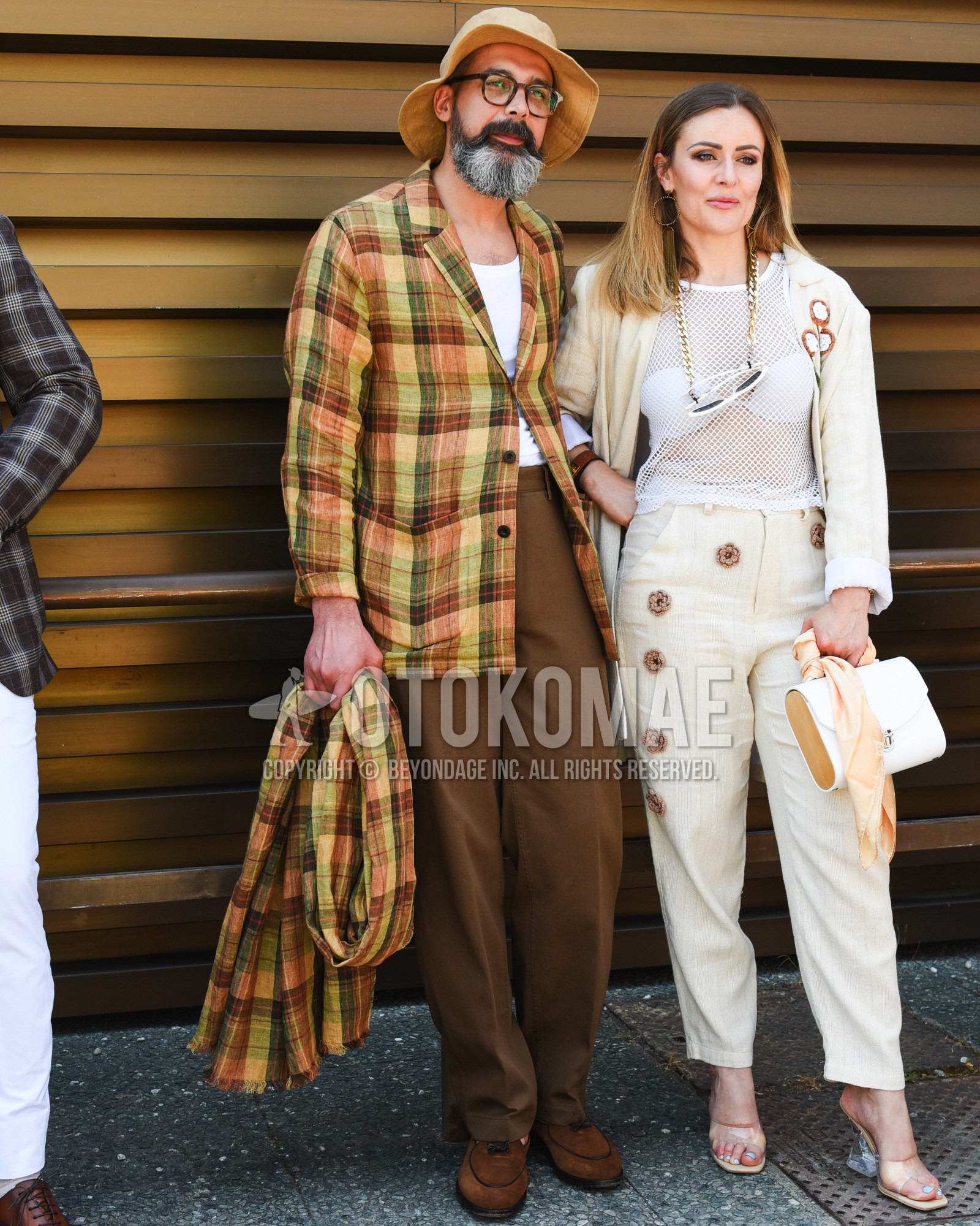 Men's spring summer outfit with beige plain bucket hat, brown tortoiseshell glasses, yellow brown check tailored jacket, white plain t-shirt, brown plain slacks, brown tassel loafers leather shoes.