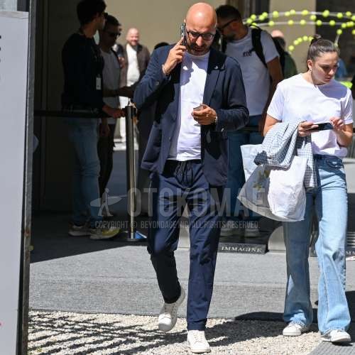 黒無地のメガネ、ネイビー無地のテーラードジャケット、白無地のTシャツ、ブルー無地のスラックス、白ローカットのスニーカーを合わせた秋春のメンズコーデ・着こなし。