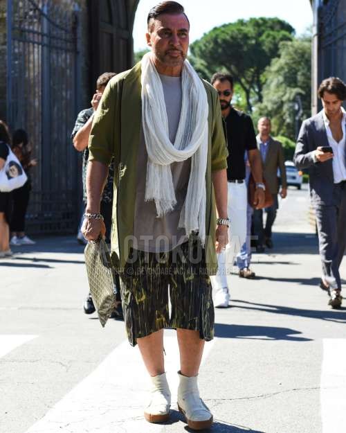 白無地のマフラー/ストール、グリーン無地のアウター、グレー無地のTシャツ、オリーブグリーン迷彩のカーゴパンツ、白のブーツ、オリーブグリーン小紋のクラッチバッグ/セカンドバッグ/巾着を合わせた夏春のメンズコーデ・着こなし。