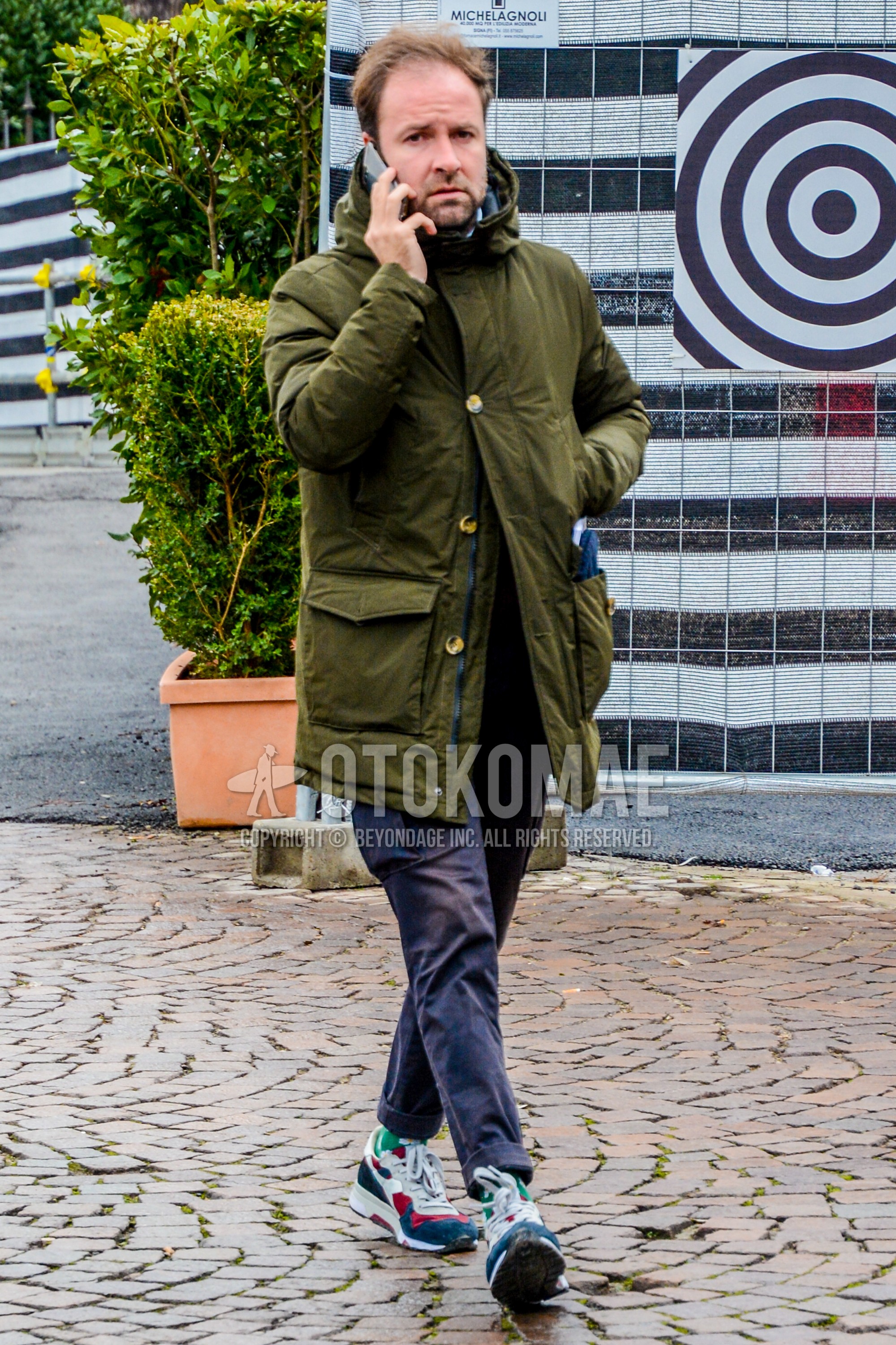 Men's winter outfit with olive green plain hooded coat, navy plain cargo pants, green plain socks, multi-color low-cut sneakers.