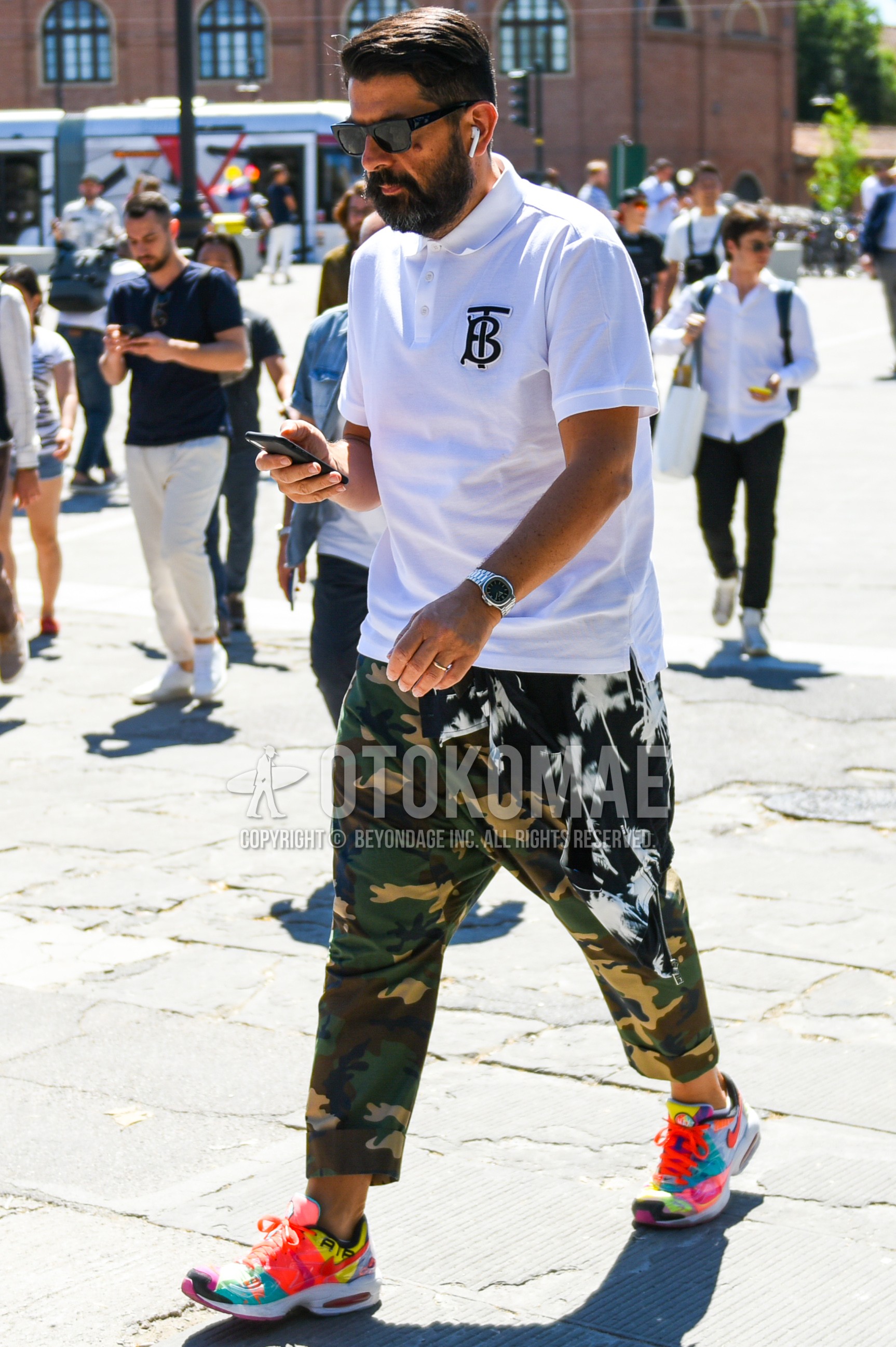Men's spring summer outfit with black plain sunglasses, white one point polo shirt, green camouflage ankle pants, multi-color low-cut sneakers.