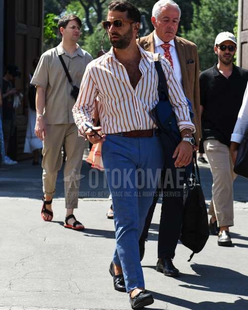 ブラウン無地のサングラス、オレンジ・白ストライプのシャツ、ブラウン無地のレザーベルト、ブルーチェックのスラックス、黒タッセルローファーの革靴、ネイビー無地のトートバッグを合わせた春夏のメンズコーデ・着こなし。