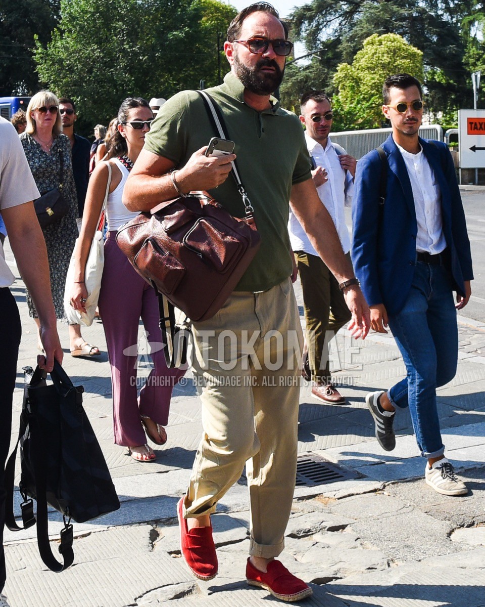 Men's spring summer outfit with brown tortoiseshell sunglasses, olive green plain polo shirt, beige plain chinos, red coin loafers leather shoes, brown plain backpack.