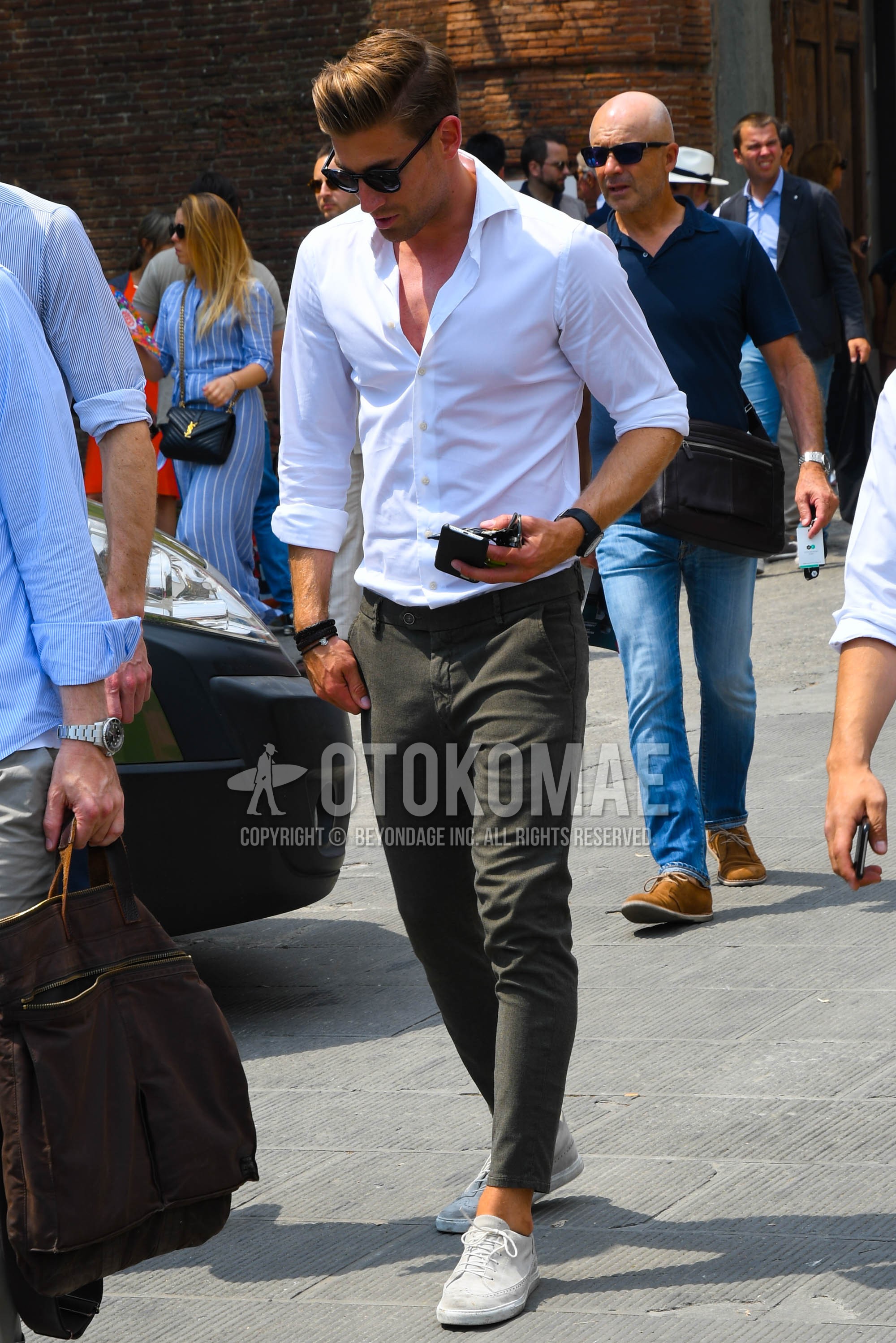 Men's spring summer outfit with black plain sunglasses, white plain shirt, gray plain chinos, white low-cut sneakers.