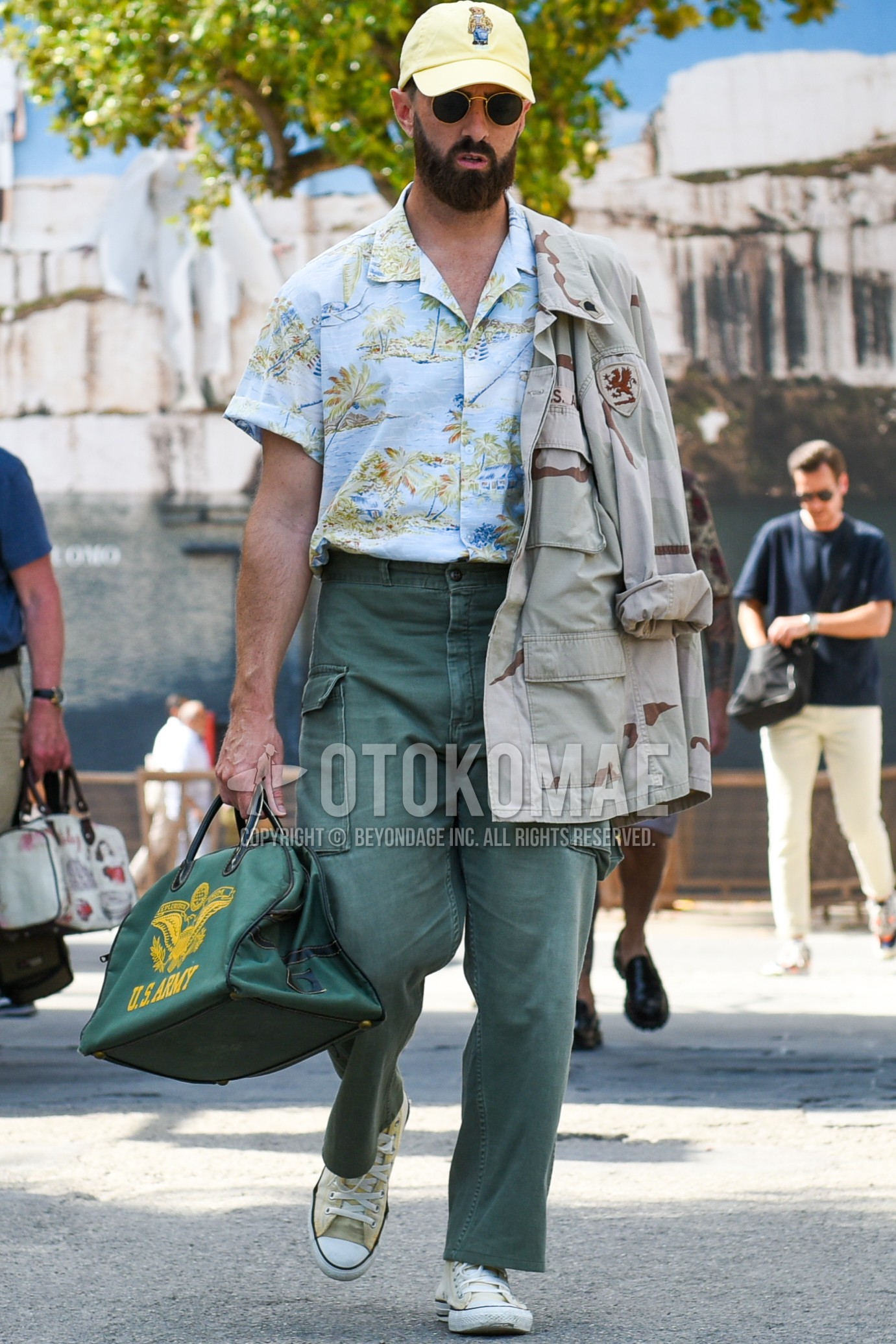 Men's spring summer autumn outfit with yellow one point baseball cap, black plain sunglasses, beige camouflage field jacket/hunting jacket, light blue tops/innerwear shirt, olive green plain cargo pants, yellow high-cut sneakers, olive green plain boston bag.