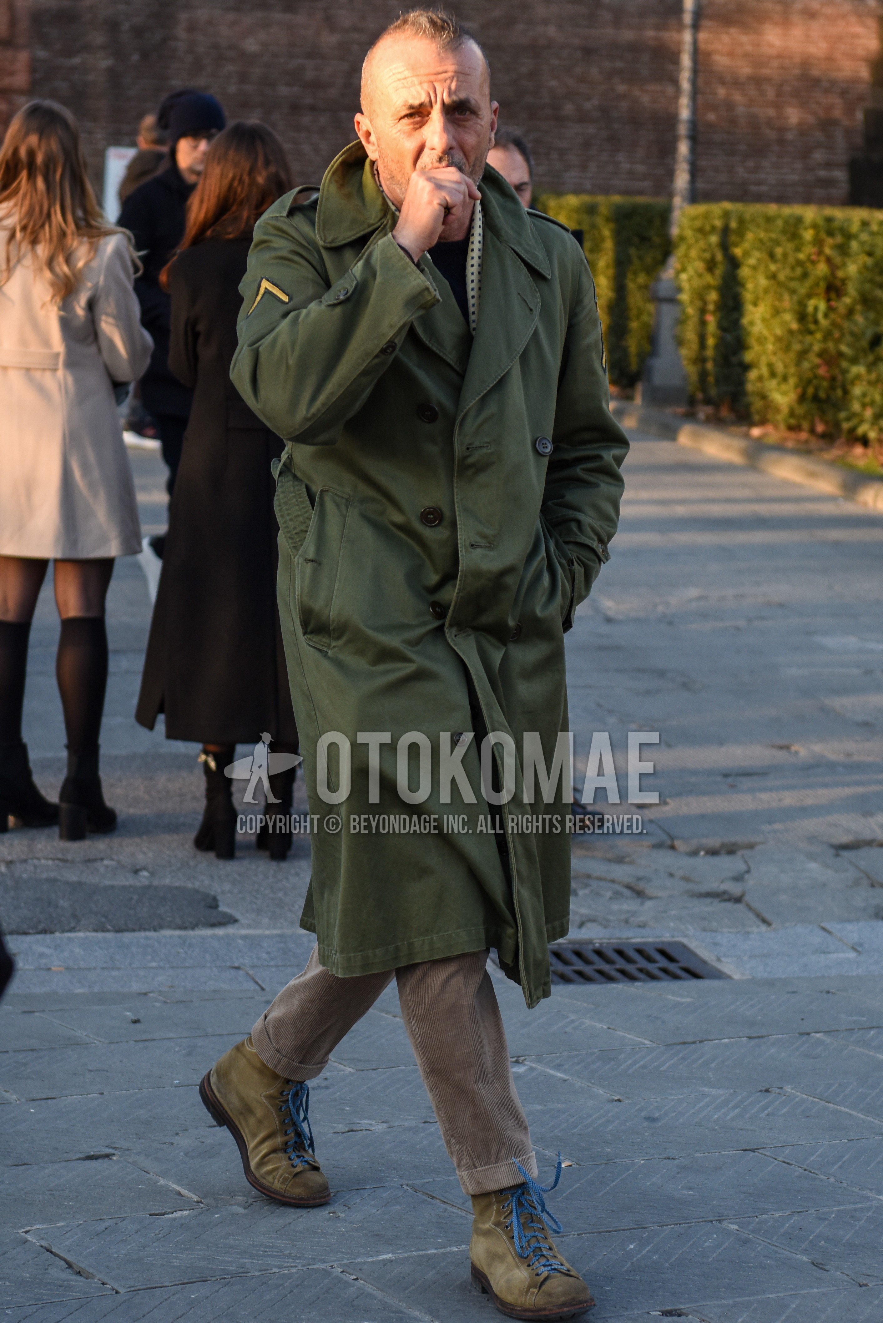 Men's autumn winter outfit with white dots scarf, olive green plain trench coat, beige plain winter pants (corduroy,velour), beige work boots.