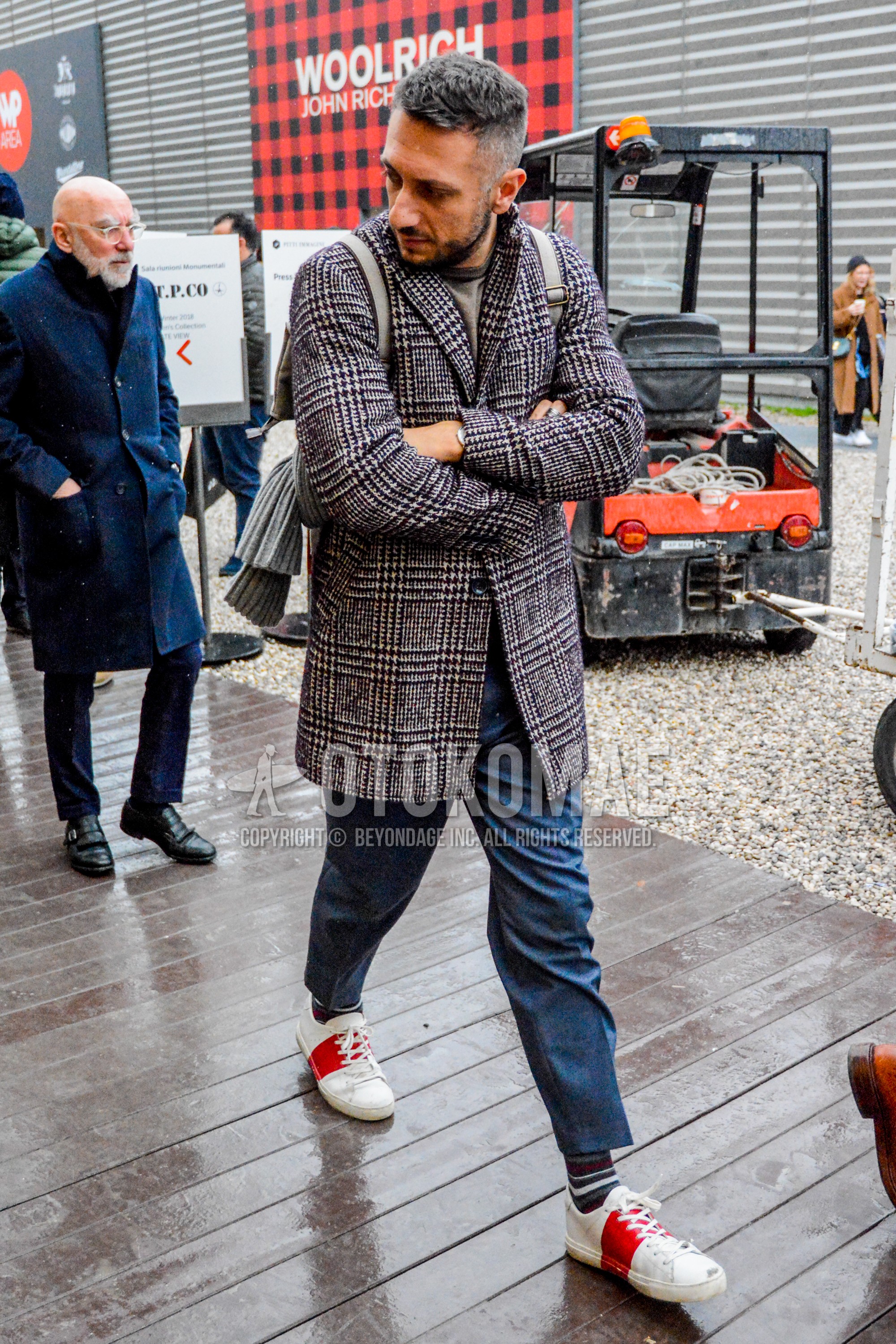 Men's autumn winter outfit with brown check chester coat, gray plain t-shirt, gray plain slacks, multi-color horizontal stripes socks, white red low-cut sneakers.