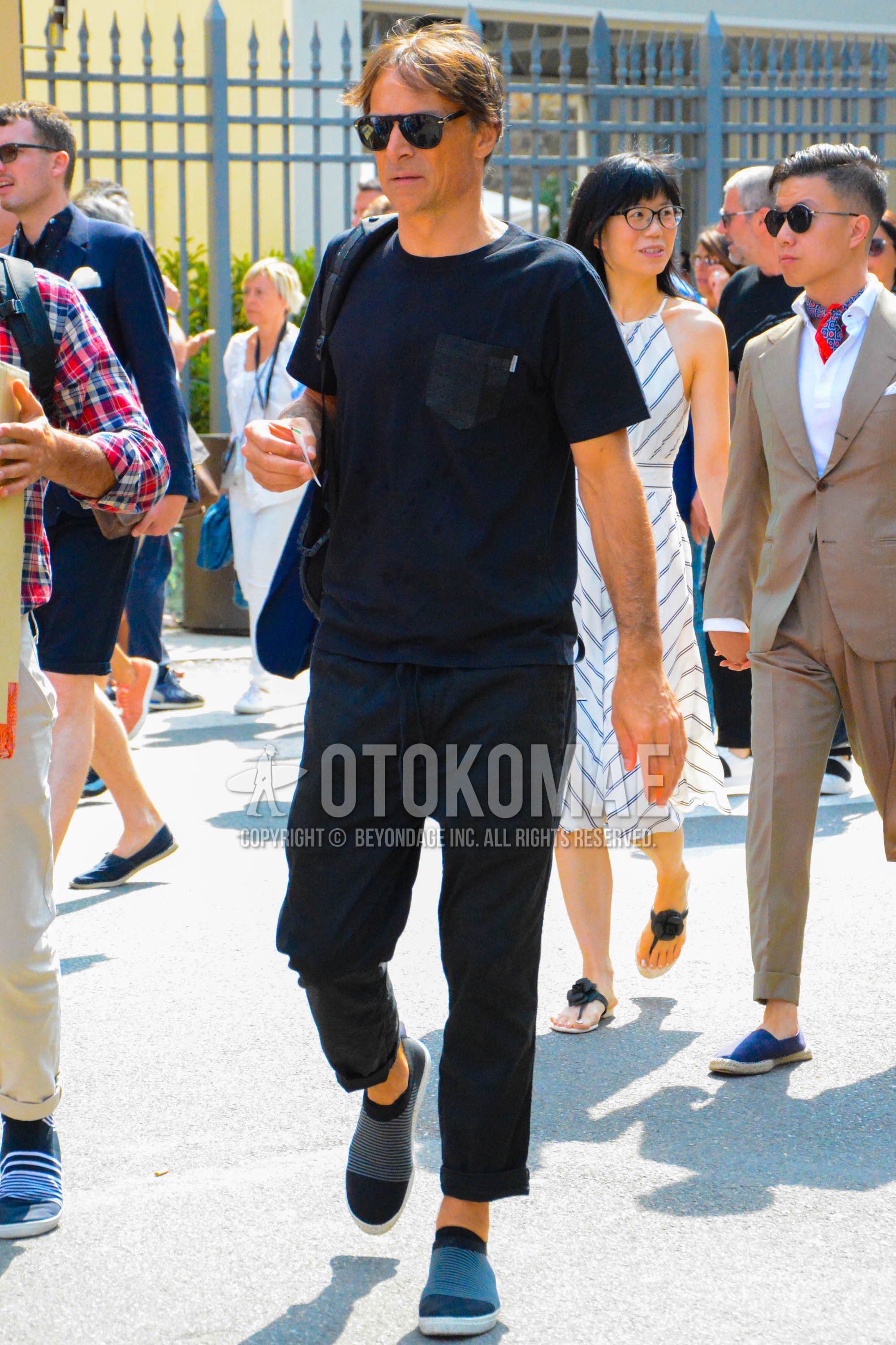 Men's spring summer outfit with black plain sunglasses, black plain t-shirt, black plain easy pants, black slip-on sneakers.