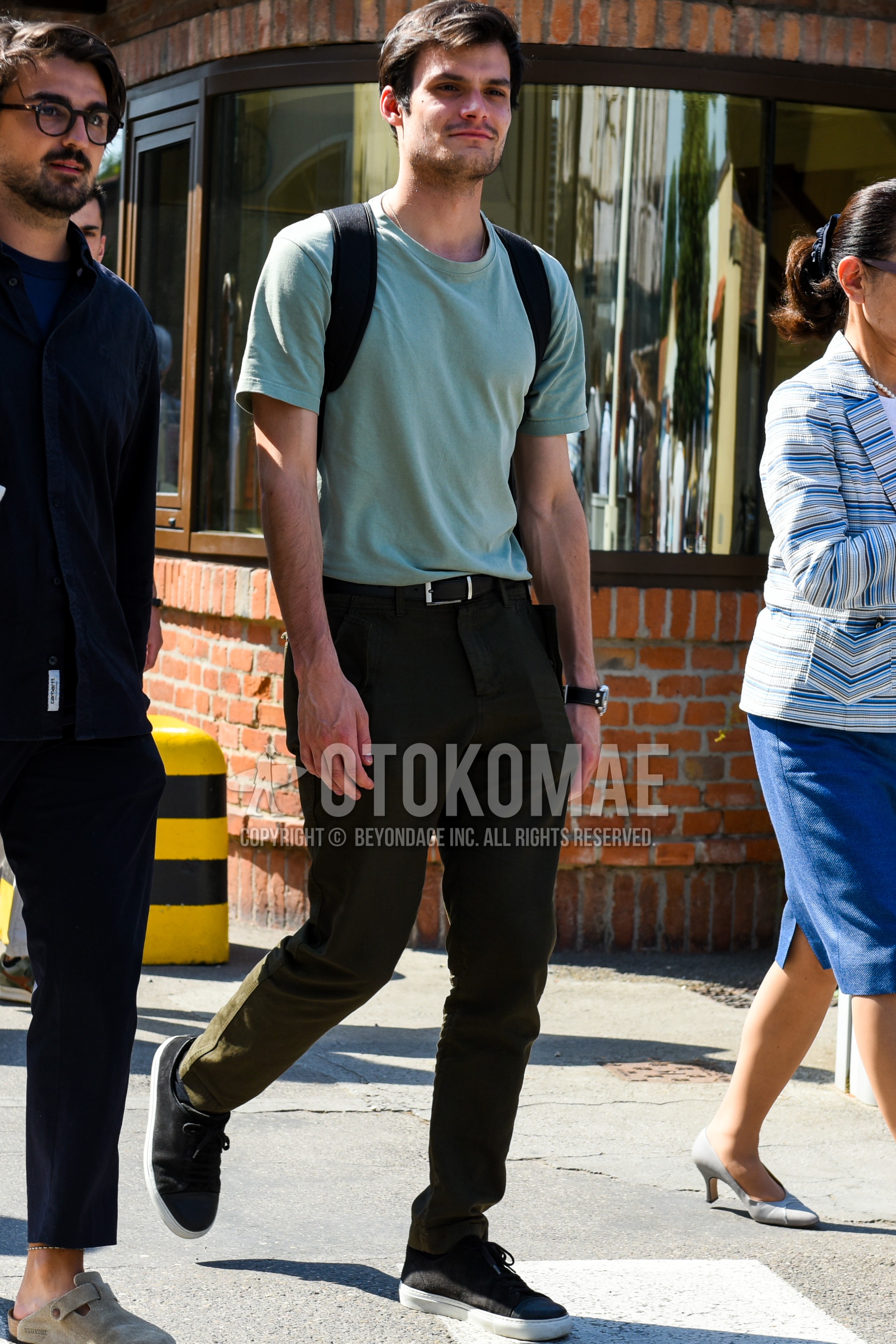 Men's spring summer outfit with green plain t-shirt, black plain leather belt, olive green plain chinos, black low-cut sneakers.