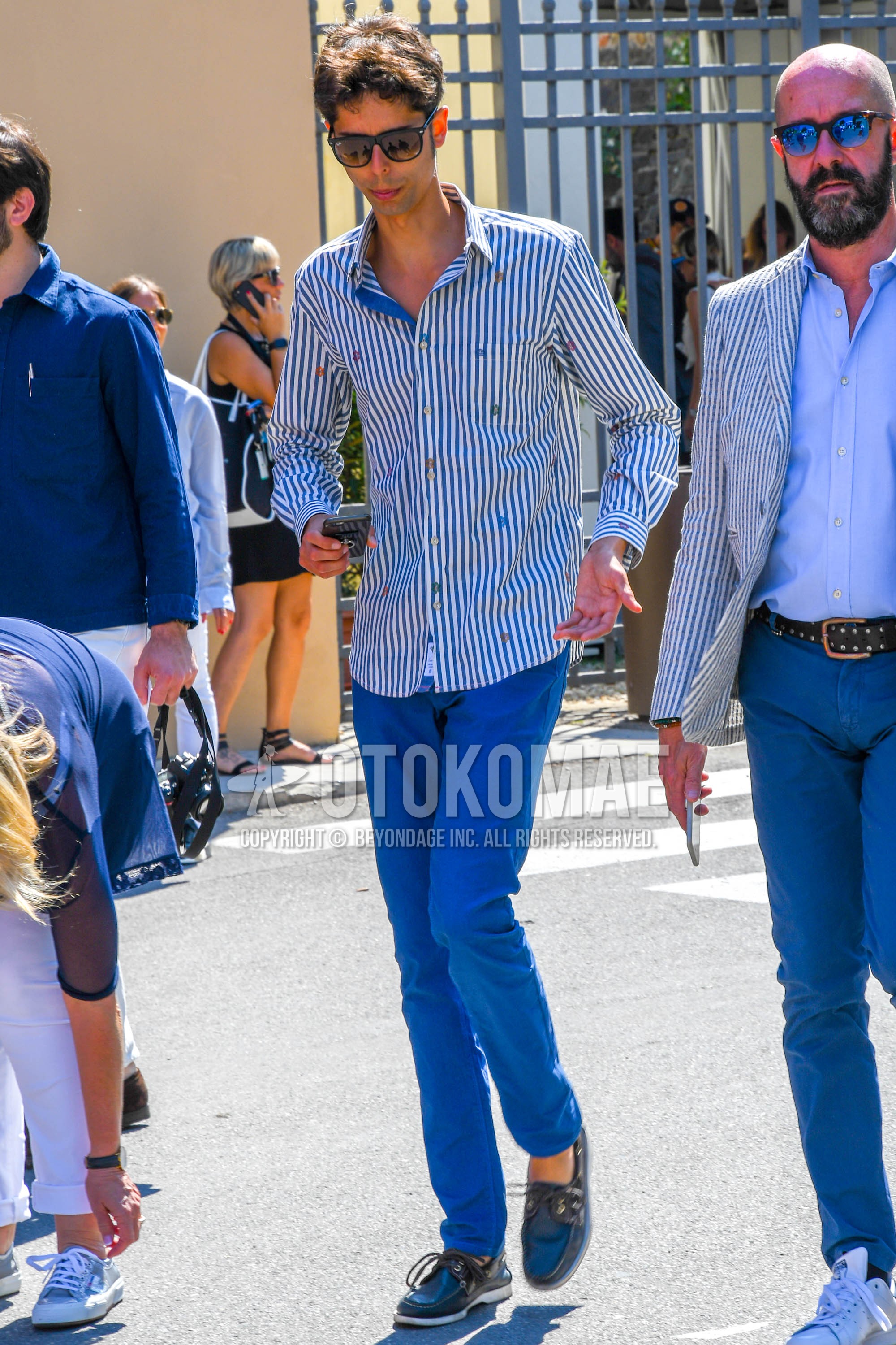 Men's spring summer outfit with plain sunglasses, white light blue stripes shirt, blue plain cotton pants, black moccasins/deck shoes leather shoes.