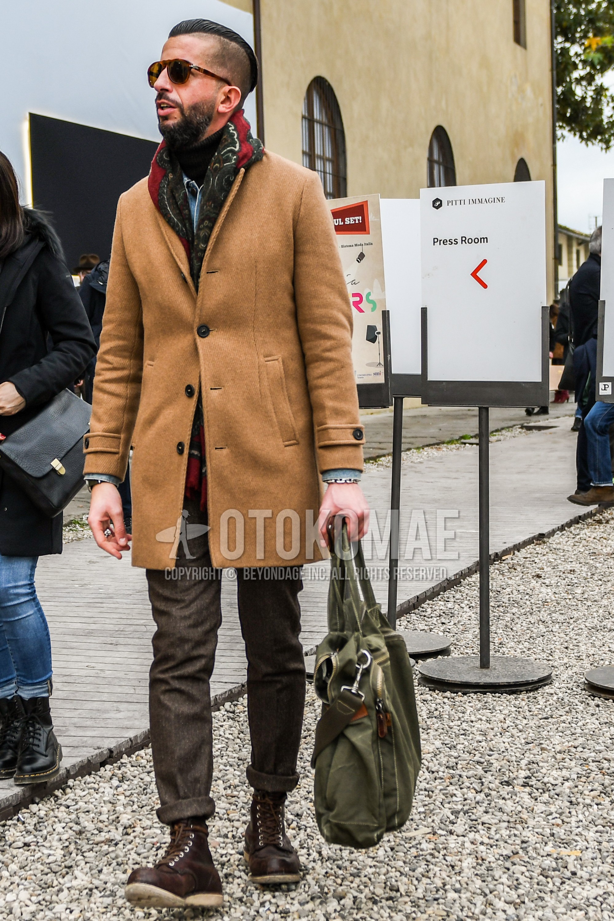 Men's autumn winter outfit with plain sunglasses, multi-color scarf scarf, beige plain chester coat, brown plain slacks, brown  boots, green plain briefcase/handbag.
