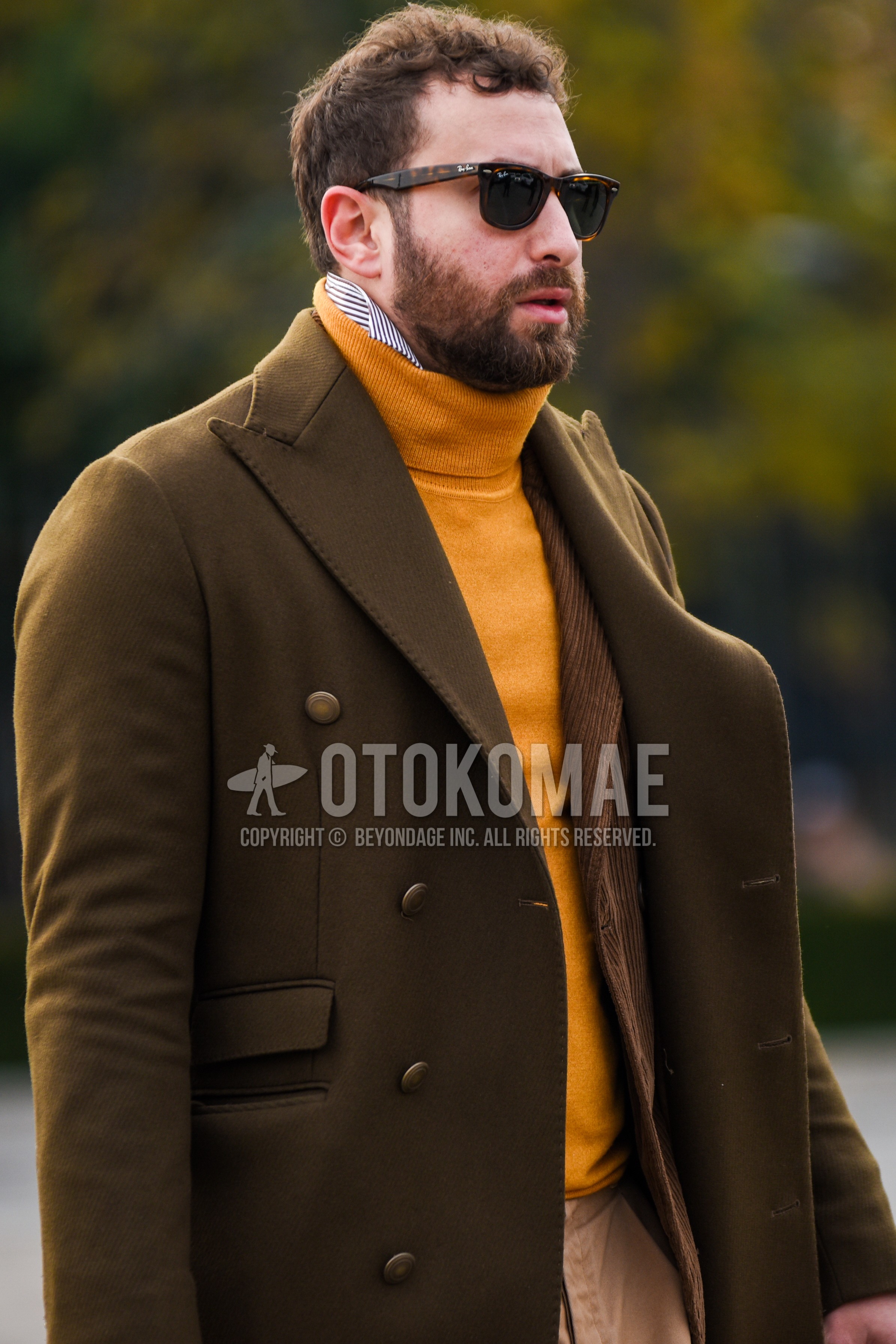 Men's autumn winter outfit with brown tortoiseshell sunglasses, olive green plain chester coat, yellow plain turtleneck knit, white blue stripes shirt, brown plain tailored jacket, beige plain chinos.