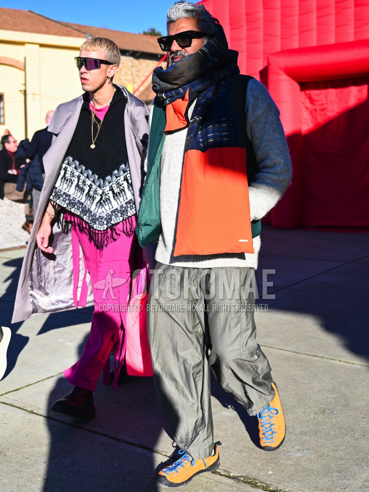 Men's autumn winter outfit with black plain sunglasses, navy orange check scarf, green plain down jacket, gray plain sweater, olive green plain cargo pants, white plain socks, yellow blue low-cut sneakers.