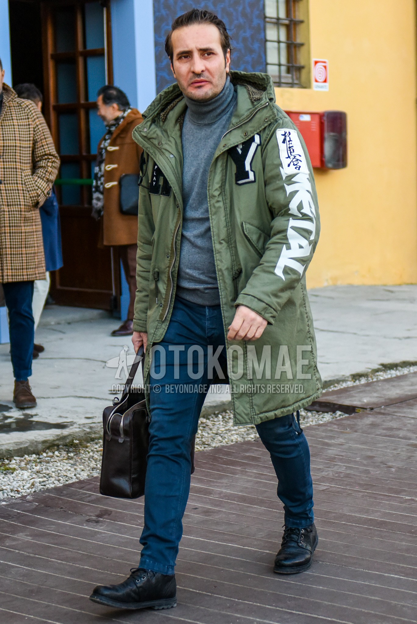 Men's winter outfit with olive green mod coat, gray plain turtleneck knit, blue plain cotton pants, black work boots, brown plain briefcase/handbag.