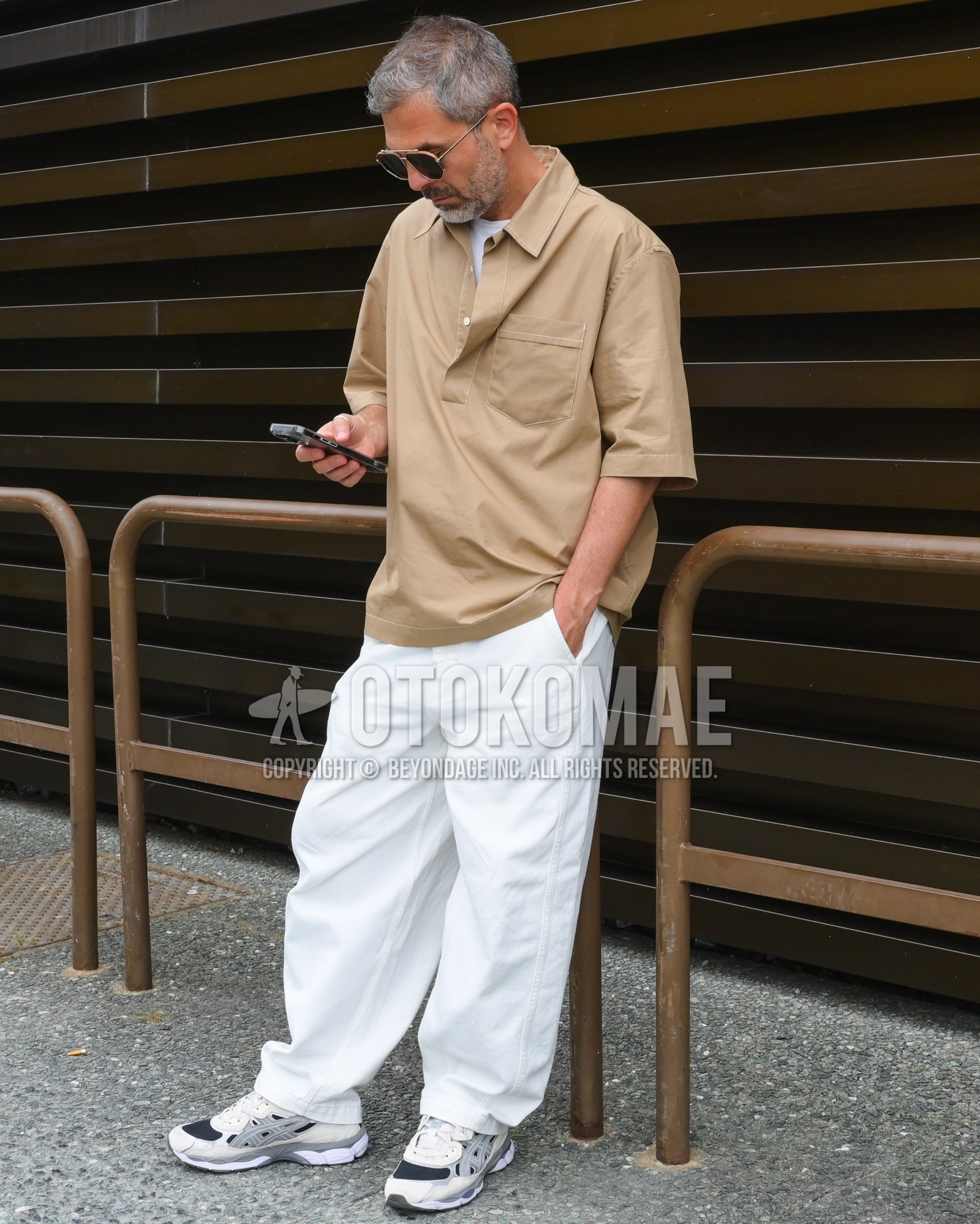 Men's spring summer outfit with black plain sunglasses, beige plain shirt, white plain t-shirt, white plain wide pants, white low-cut sneakers.