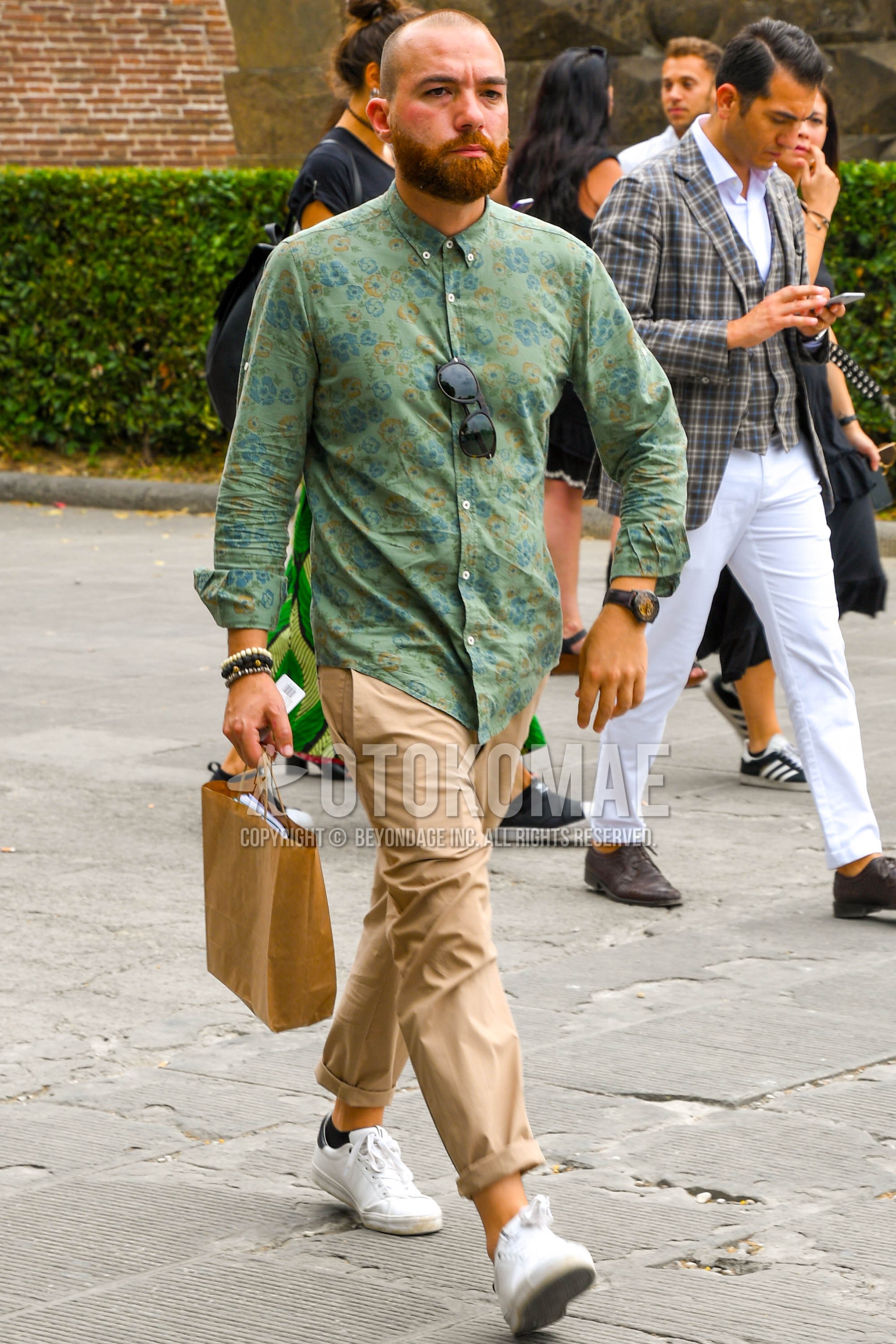 Men's spring summer autumn outfit with green botanical shirt, beige plain chinos, white low-cut sneakers.