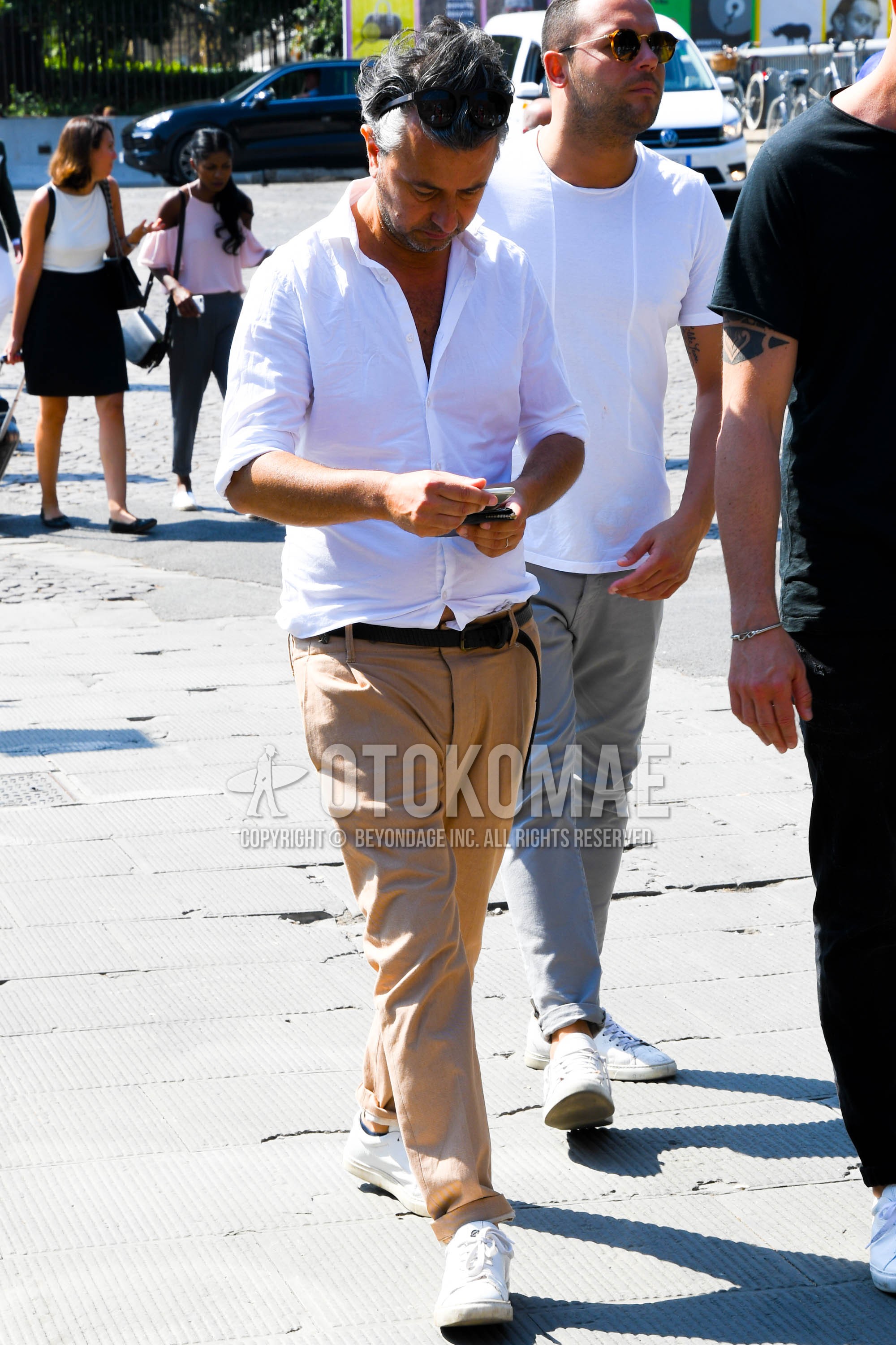 Men's spring summer outfit with white plain shirt, black plain leather belt, beige plain chinos, white low-cut sneakers.