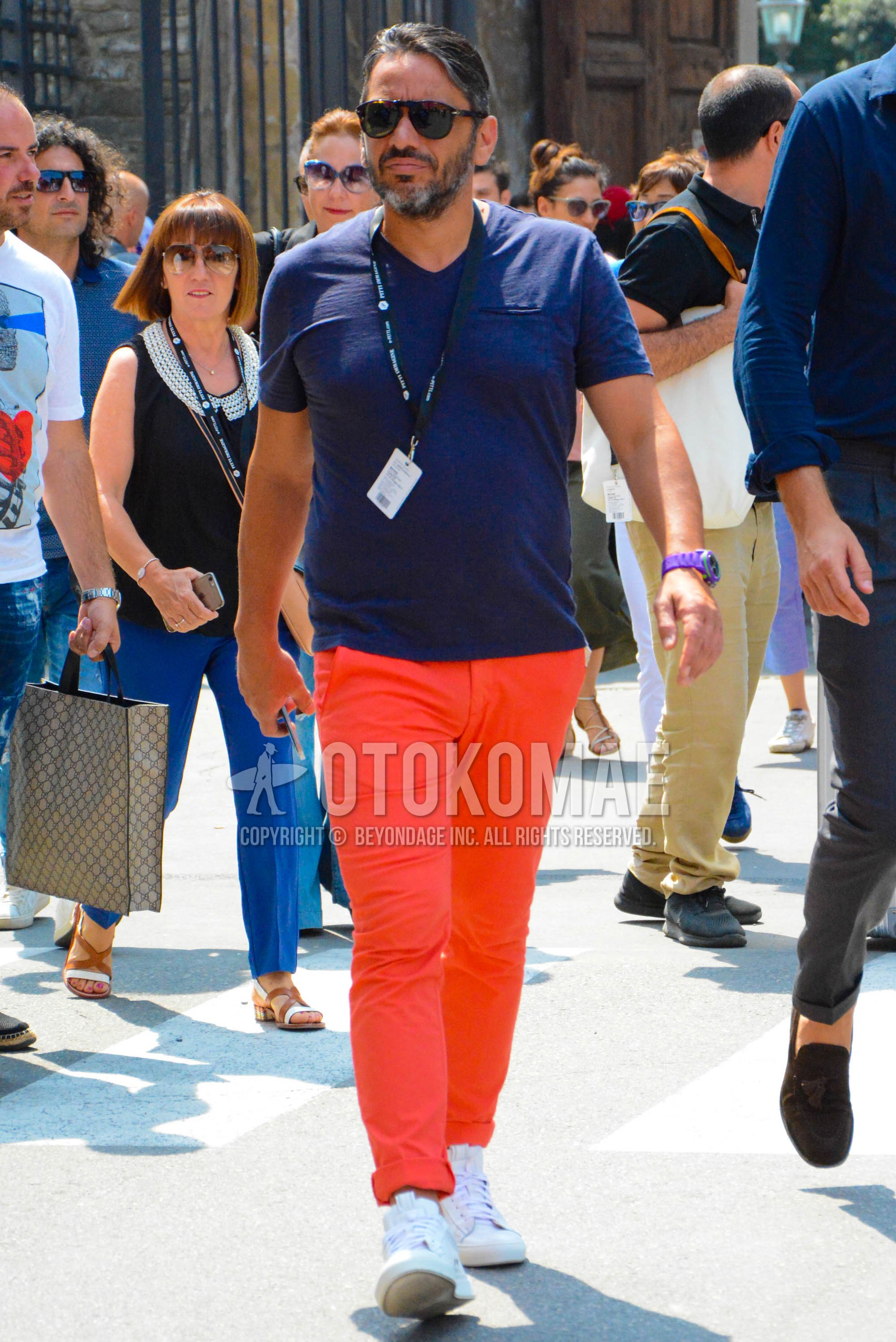 Men's spring summer outfit with brown tortoiseshell sunglasses, navy plain t-shirt, orange plain chinos, white high-cut sneakers.