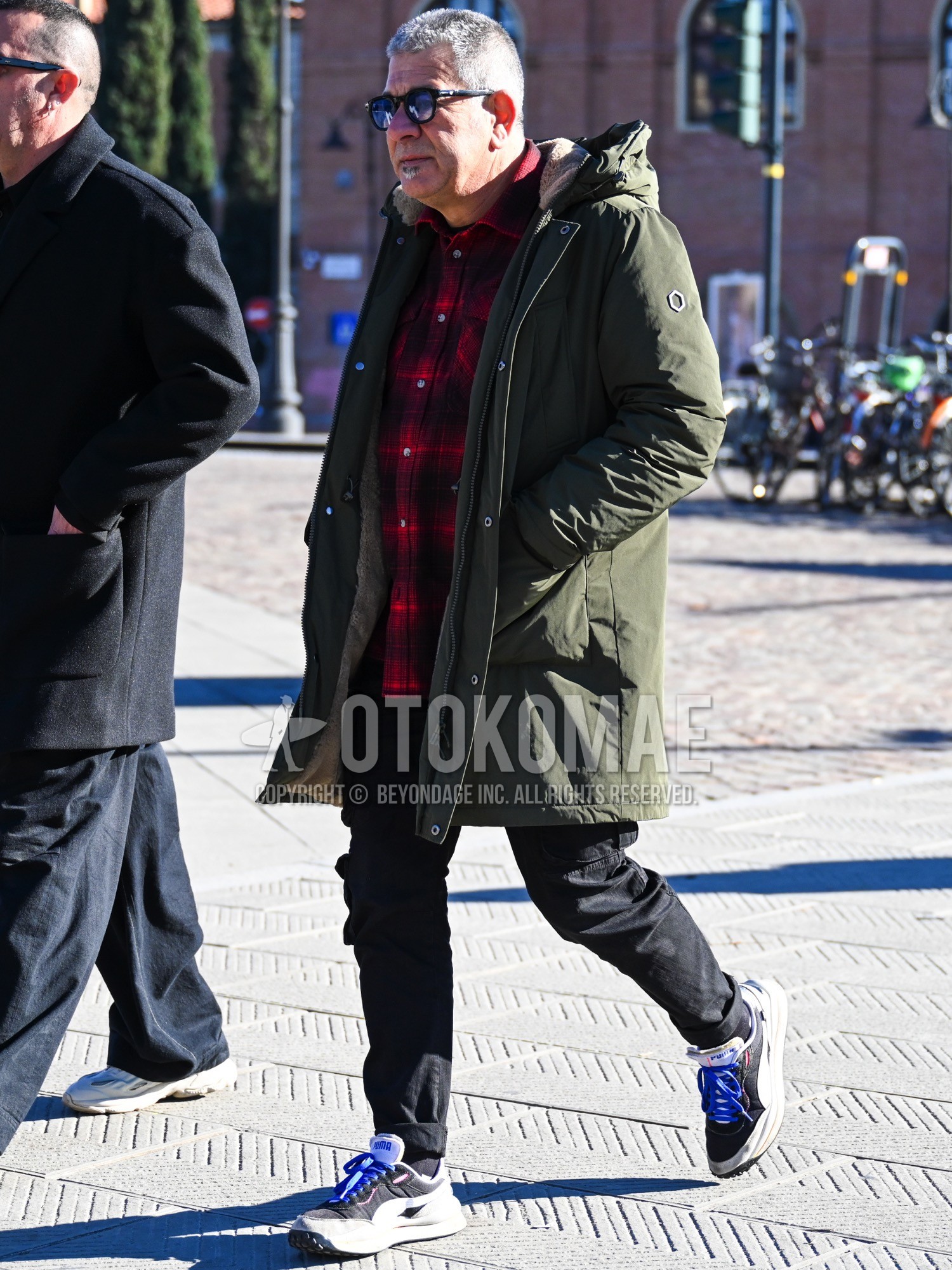 Men's autumn winter outfit with black plain sunglasses, olive green plain mod coat, red check shirt, black plain cargo pants, black plain socks, black white low-cut sneakers.
