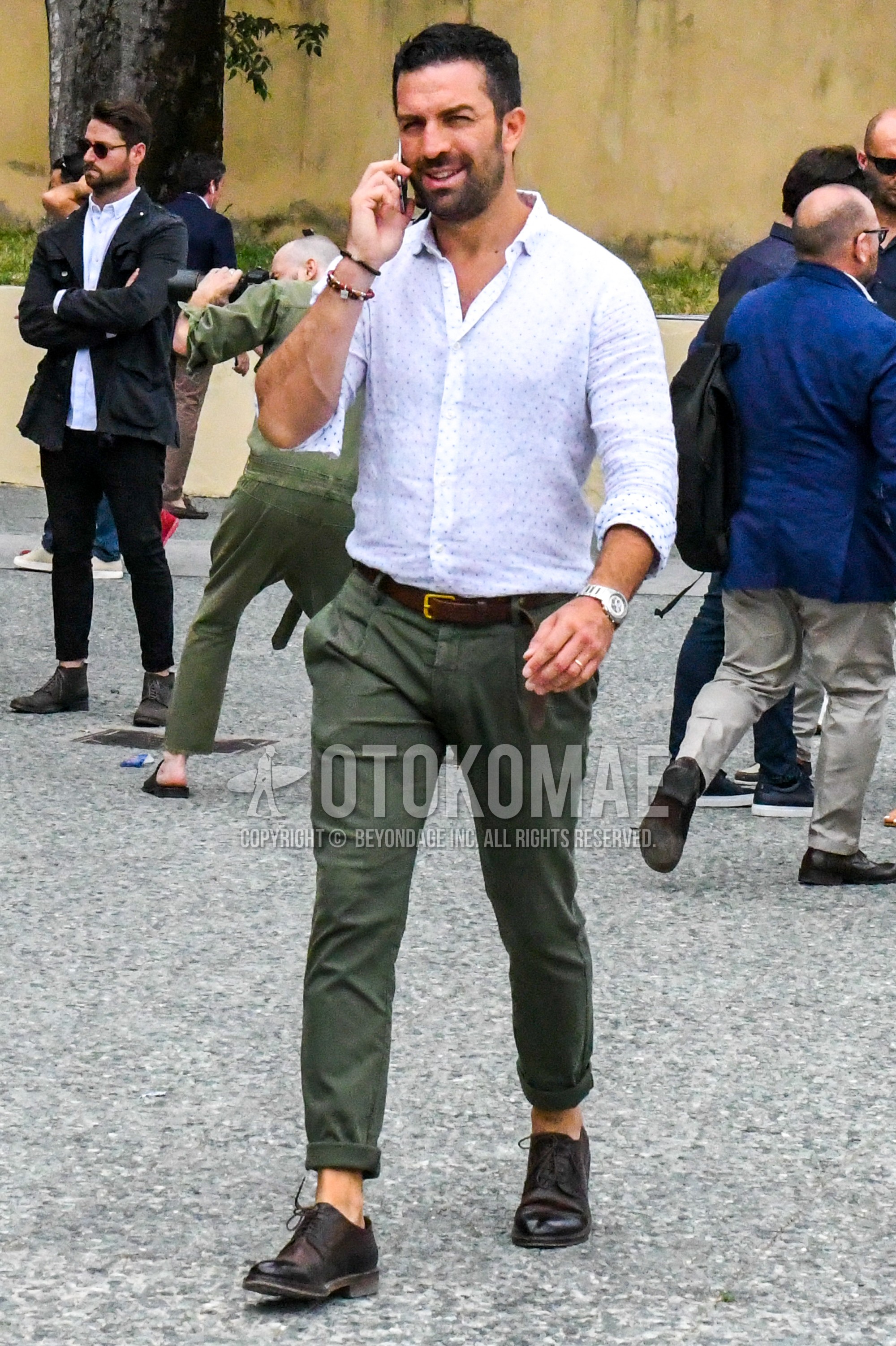 Men's spring summer outfit with white dots shirt, brown plain leather belt, olive green plain chinos, olive green plain pleated pants, brown straight-tip shoes leather shoes.