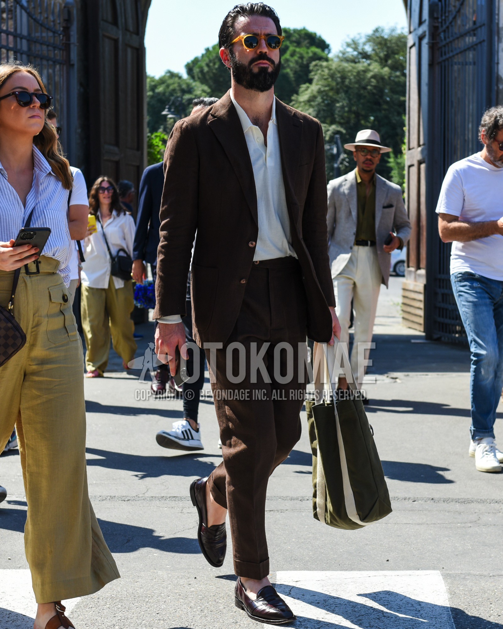 Men's spring summer outfit with yellow plain sunglasses, beige plain polo shirt, brown coin loafers leather shoes, olive green plain tote bag, brown plain suit.
