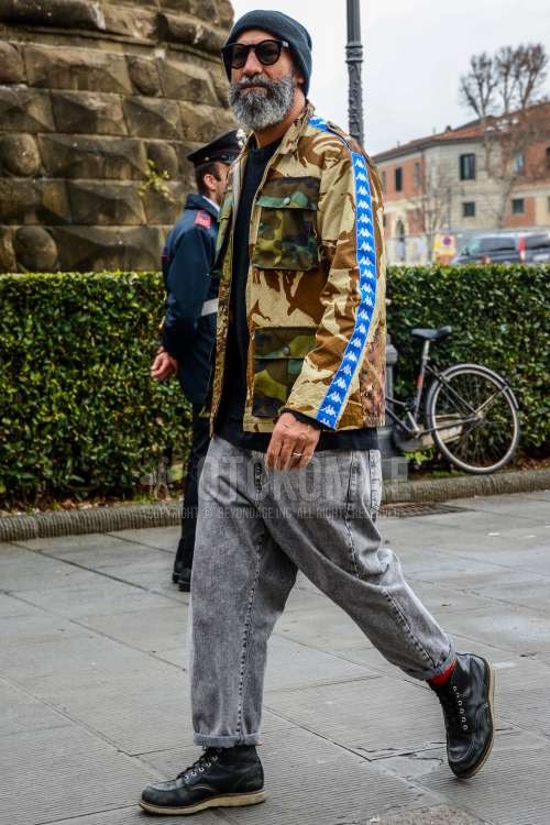 無地のニットキャップ、無地のサングラス、カッパのブラウン・ベージュ迷彩のM-65、黒無地のセーター、グレー無地のデニム/ジーンズ、レッド無地のソックス、黒ワークのブーツを合わせた秋冬のメンズコーデ・着こなし。