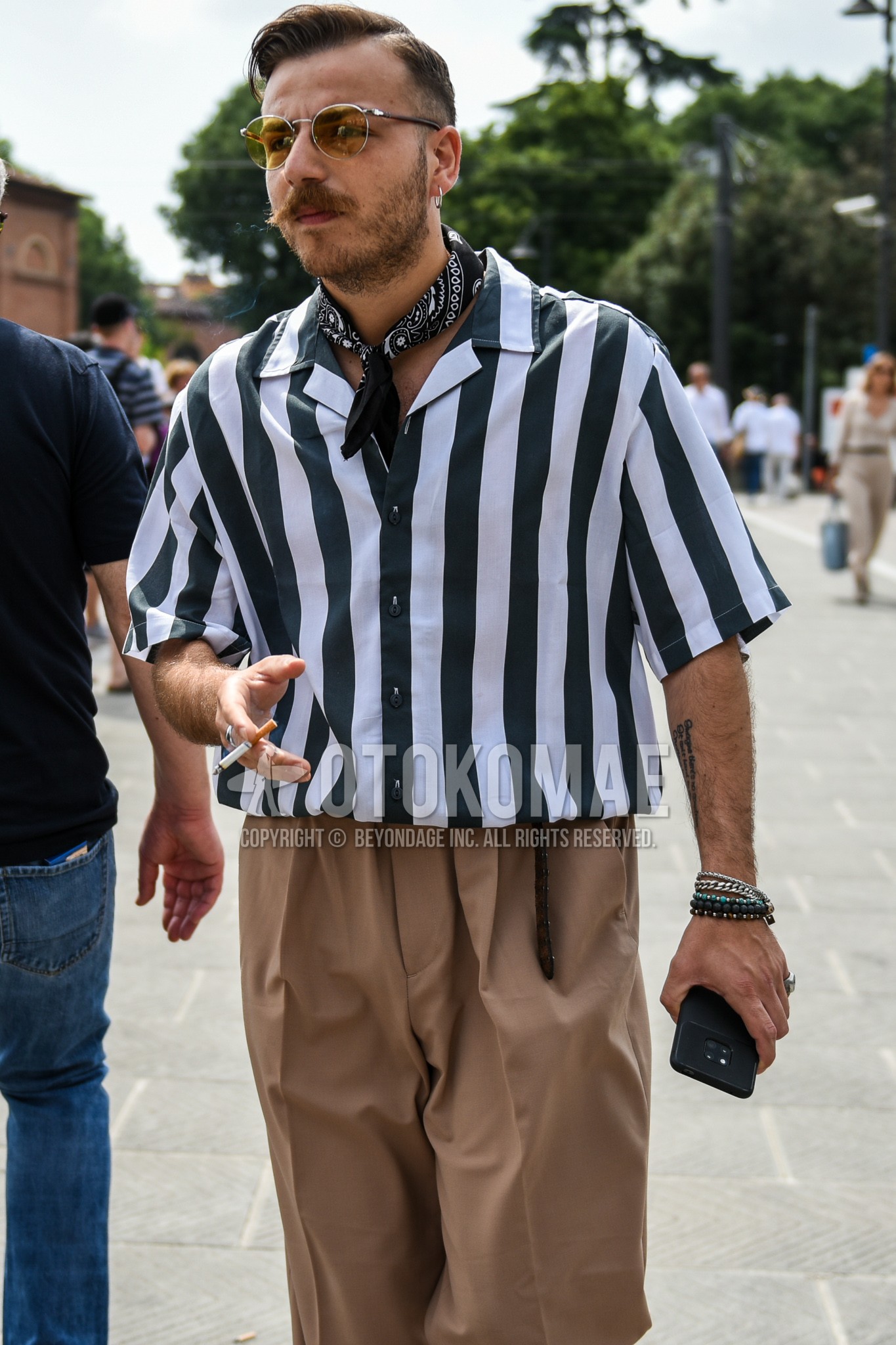 Men's summer outfit with beige plain sunglasses, black paisley bandana/neckerchief, white black stripes shirt, beige plain pleated pants, plain slacks.
