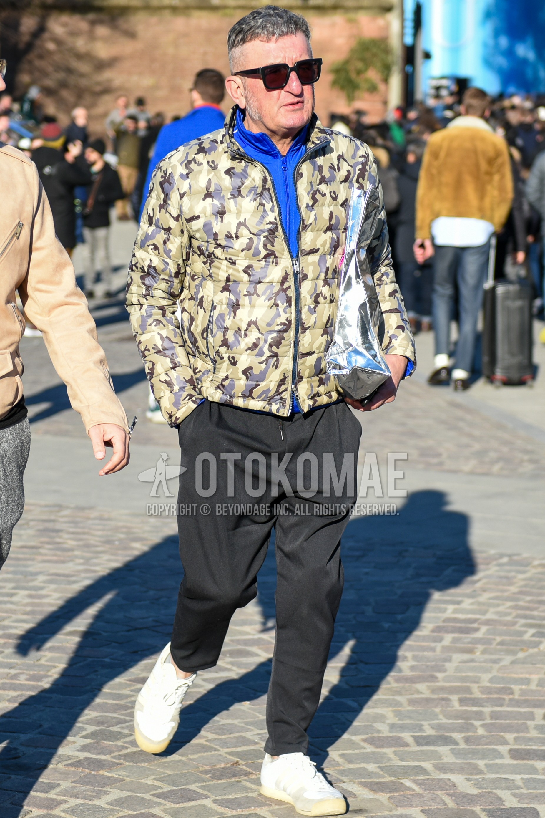 Men's autumn winter outfit with black plain sunglasses, beige camouflage down jacket, blue plain inner down, black plain easy pants, white low-cut sneakers.