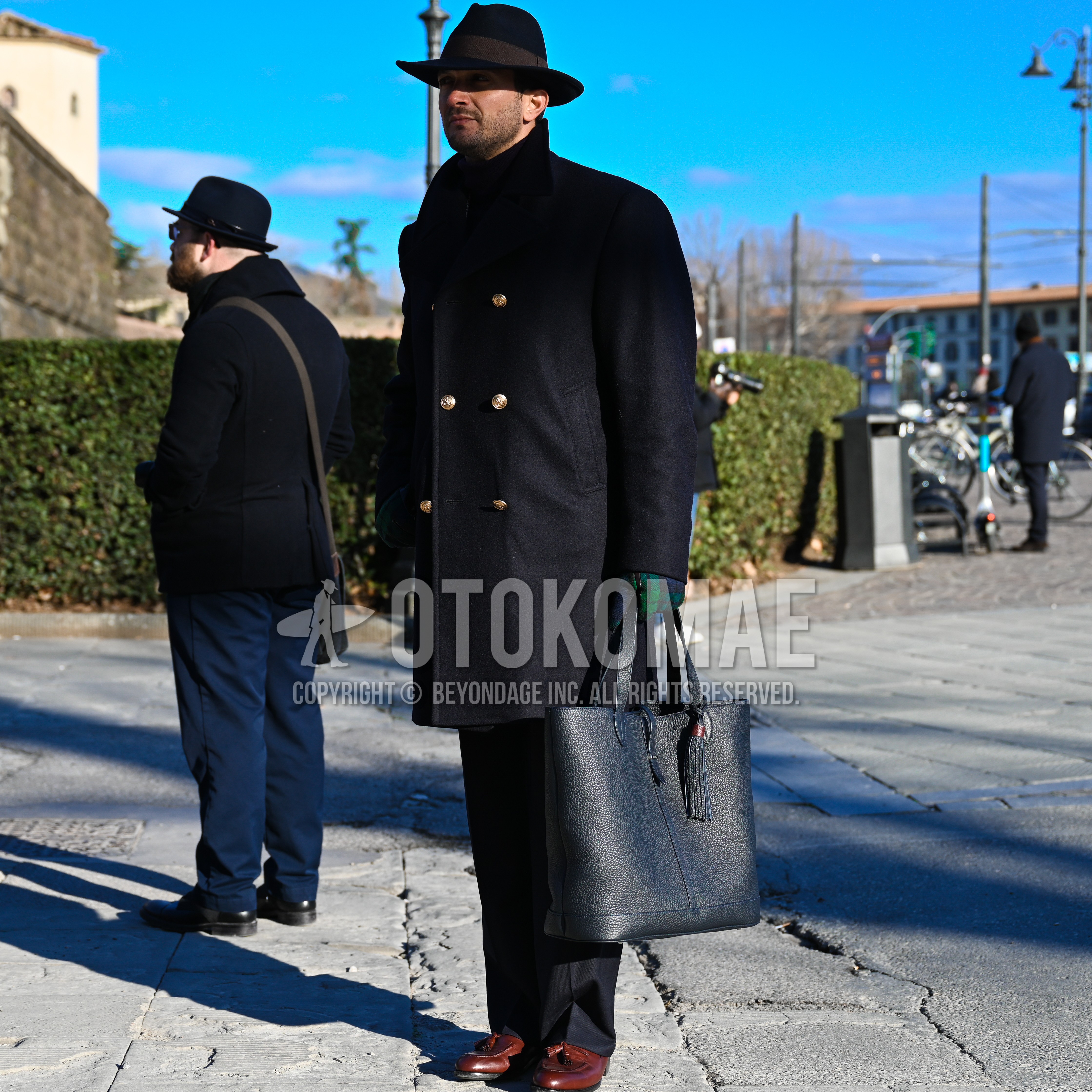 Men's autumn winter outfit with black plain hat, black plain ulster coat, black plain slacks, brown tassel loafers leather shoes, black plain tote bag.