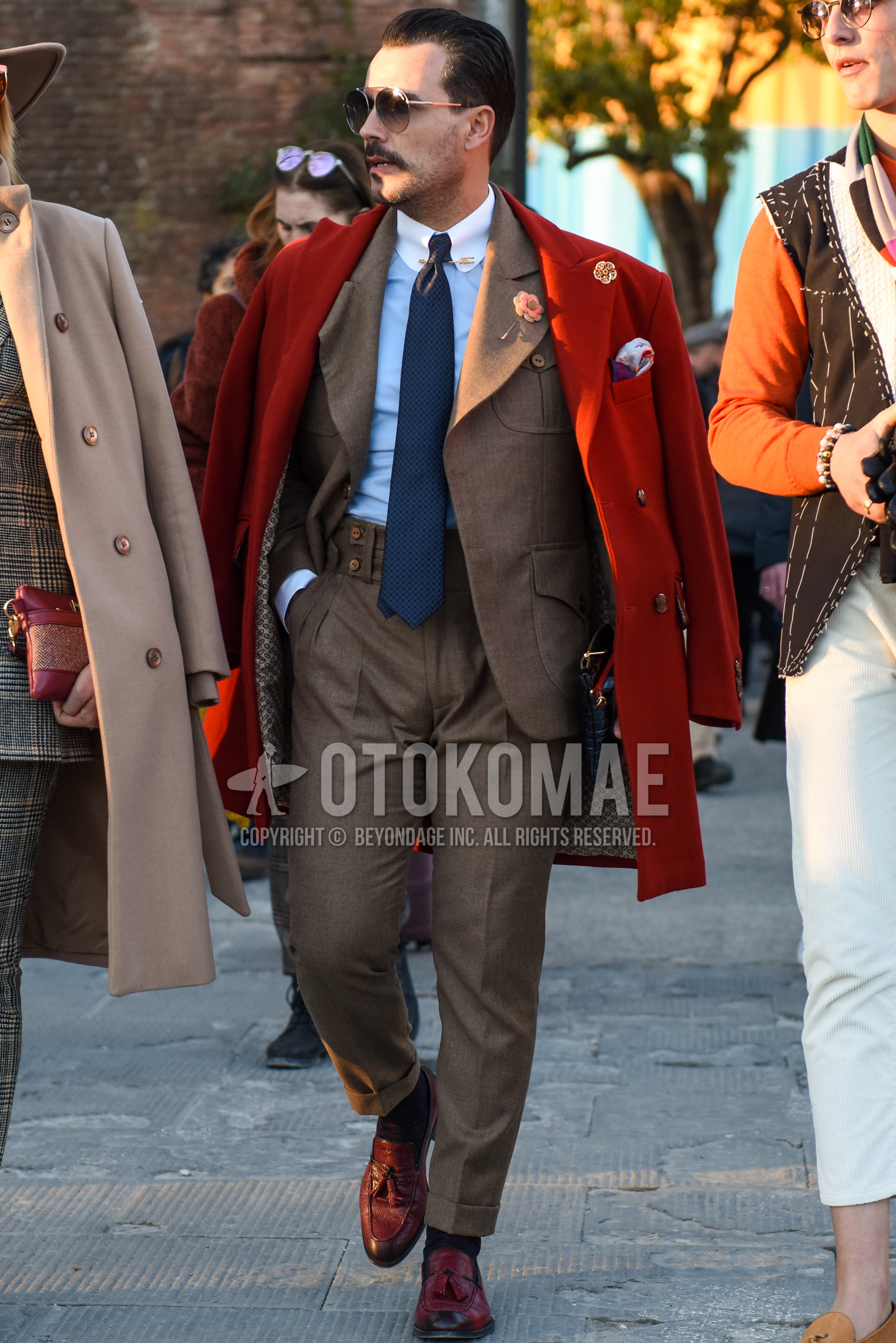 Men's autumn winter outfit with silver plain sunglasses, orange plain chester coat, black plain socks, brown tassel loafers leather shoes, beige plain casual setup, gray necktie necktie.