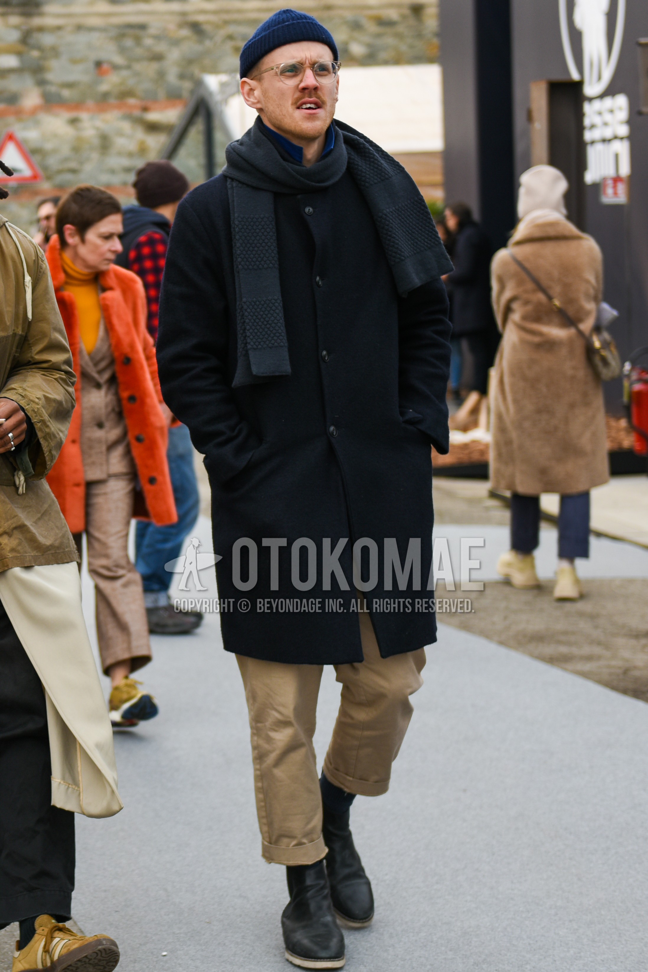 Men's autumn winter outfit with navy plain knit cap, clear plain glasses, dark gray plain scarf, black plain stenkarrer coat, beige plain chinos, black side-gore boots.
