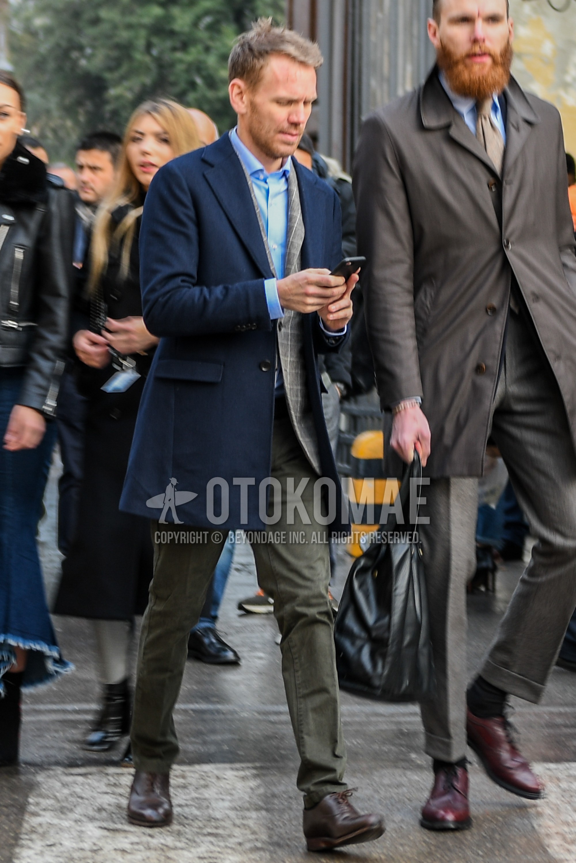 Men's winter outfit with navy plain chester coat, gray check tailored jacket, light blue plain shirt, olive green plain cotton pants, brown plain toe leather shoes.