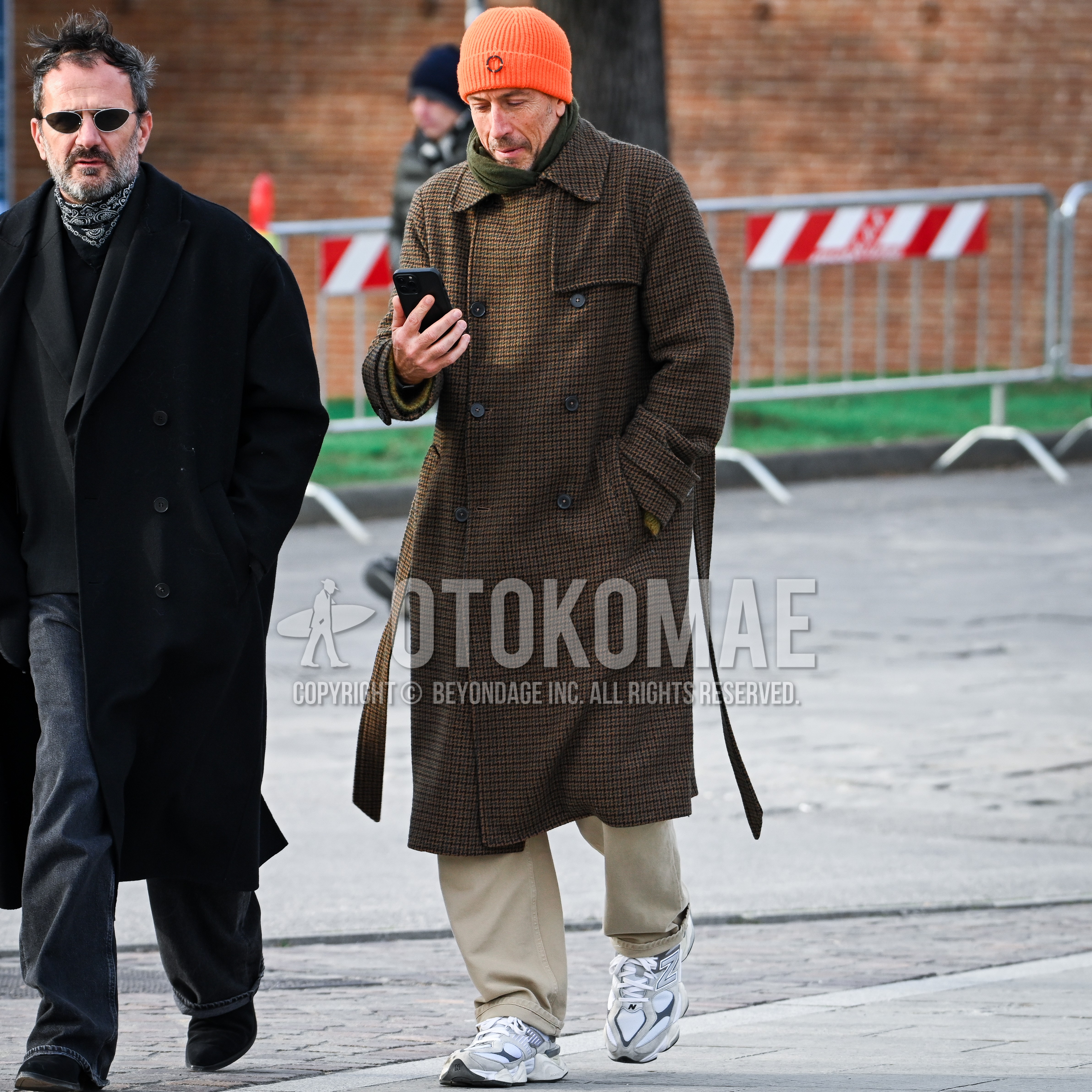 Men's autumn winter outfit with orange one point knit cap, olive green plain scarf, brown check p coat, beige plain chinos, gray low-cut sneakers.