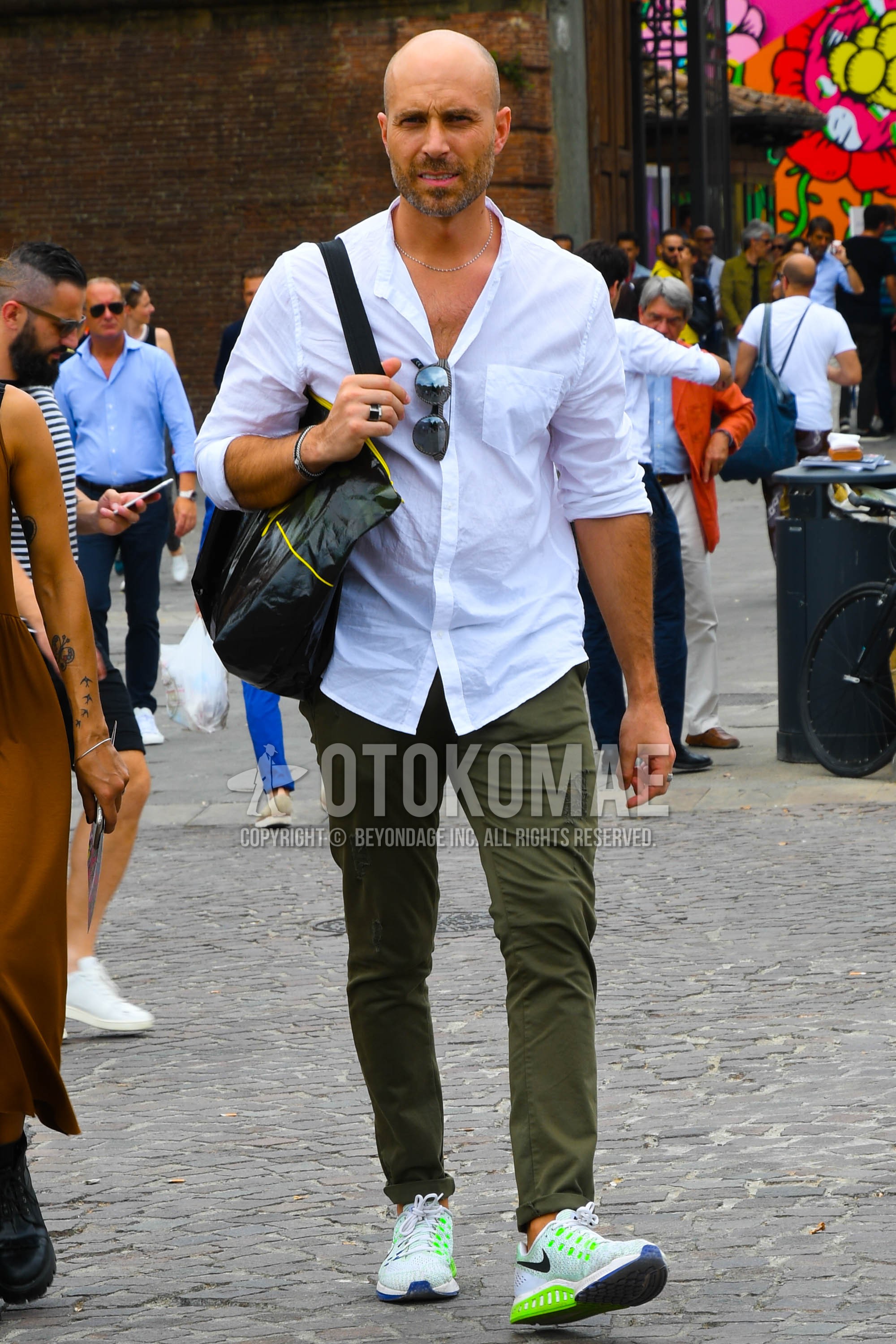 Men's spring summer outfit with white plain shirt, olive green plain chinos, white low-cut sneakers.