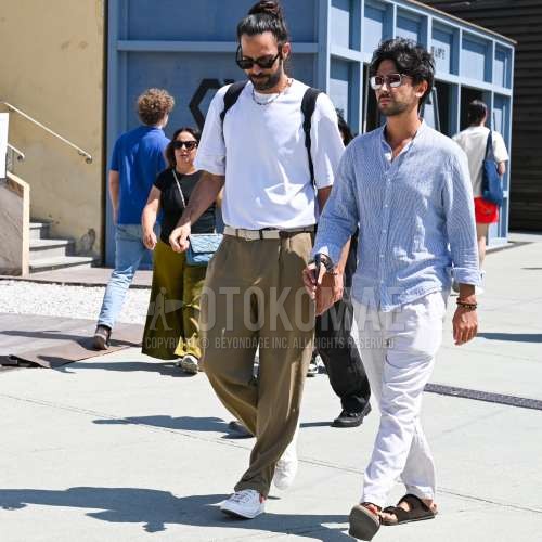 ブラウンべっ甲のサングラス、白無地のTシャツ、白無地のメッシュベルト、ベージュ無地のスラックス、ベージュ無地のプリーツパンツ、白ローカットのスニーカー、黒無地のバックパックを合わせた夏春のメンズコーデ・着こなし。