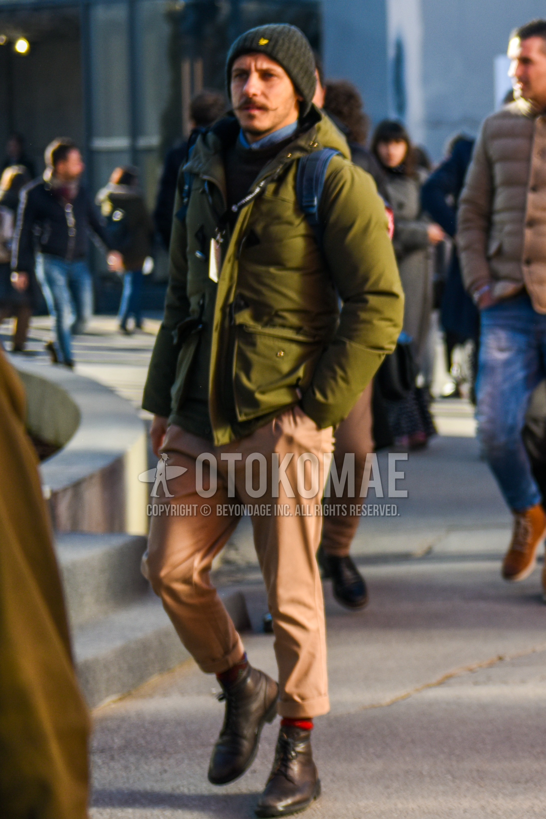 Men's winter outfit with dark gray plain knit cap, olive green plain down jacket, black plain sweater, beige plain chinos, red horizontal stripes socks, brown  boots.